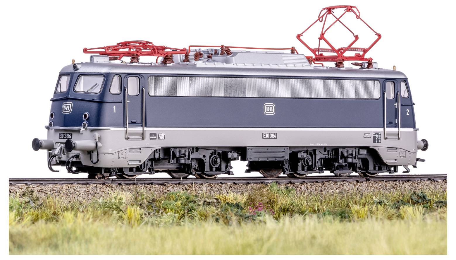 Eine Modelleisenbahn-Lokomotive auf einem Gleis mit einer grasigen Landschaft, die detaillierte Elemente wie rote Oberleitung und ein zweifarbiges Farbschema zeigt.