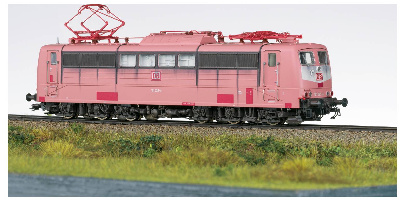 Ein Modell eines hellrosa elektrischen Zuges mit dem DB-Logo, auf Schienen mit Gras in der Nähe, unter einem klaren Himmel.
