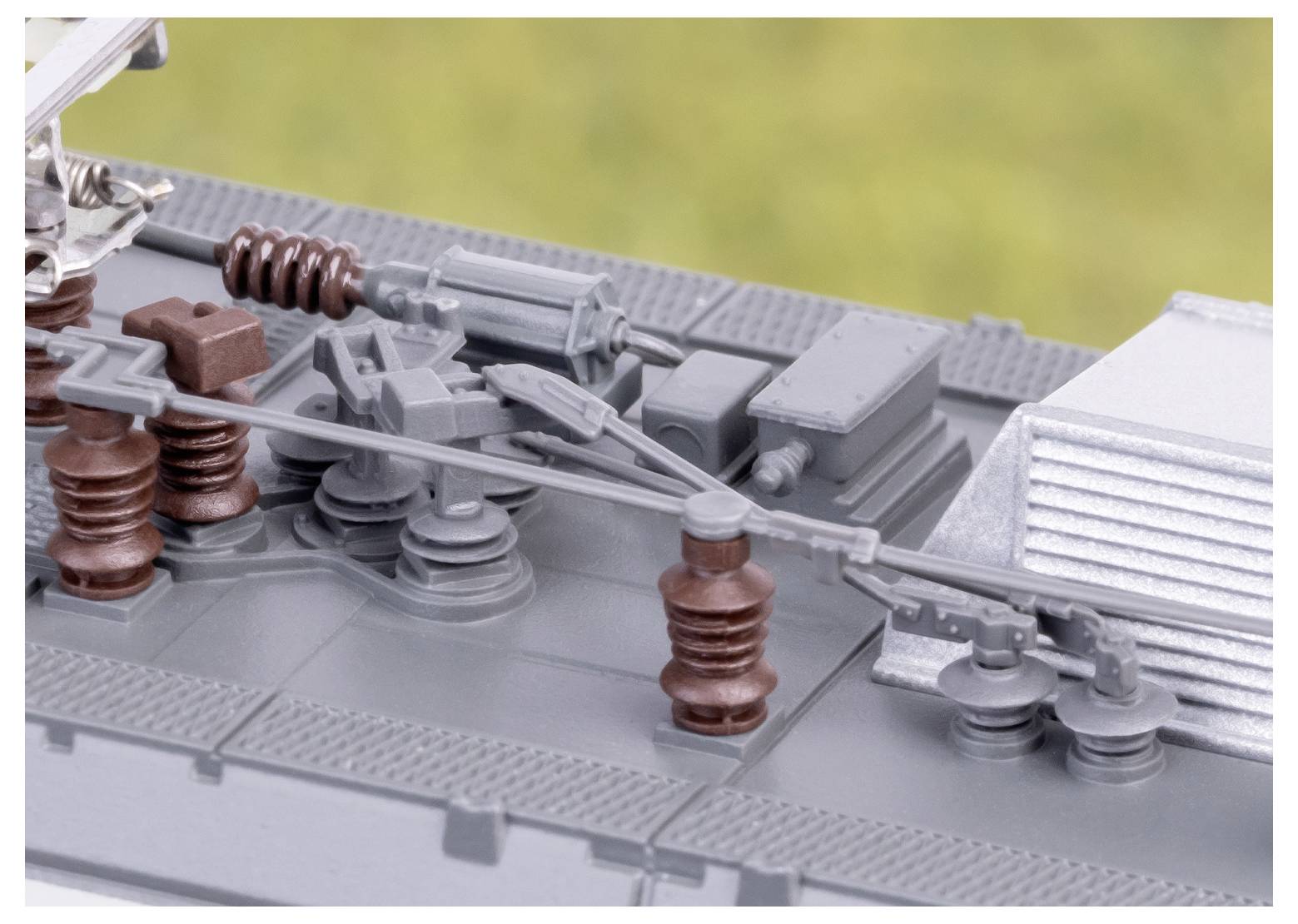 Detailaufnahme eines Modellzugdachs, das verschiedene mechanische Komponenten wie Stangen, Isolatoren und elektrische Ausrüstung zeigt, vor einem unscharfen Hintergrund.