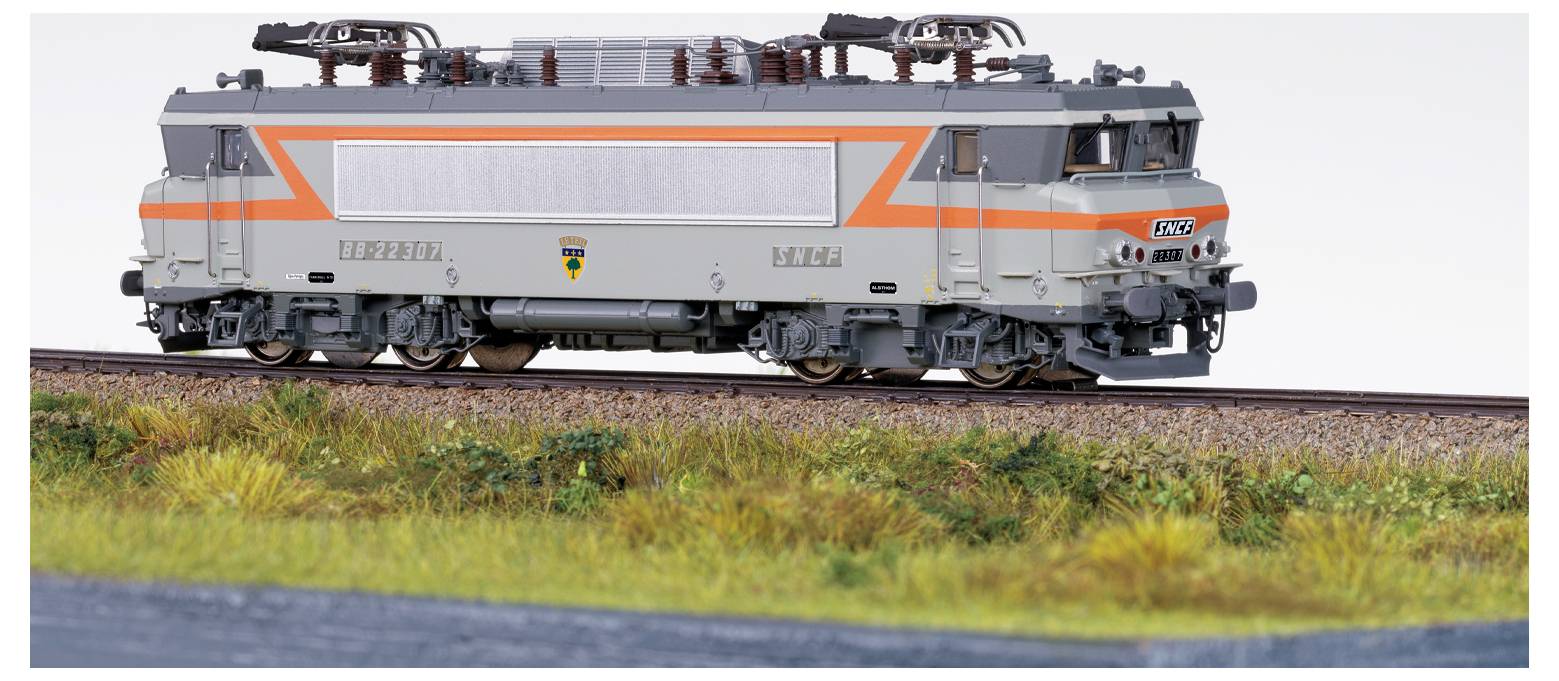 Eine Modelleisenbahn-Lokomotive mit orange und grauen Details fährt auf einer Strecke in einer Gralandschaft.