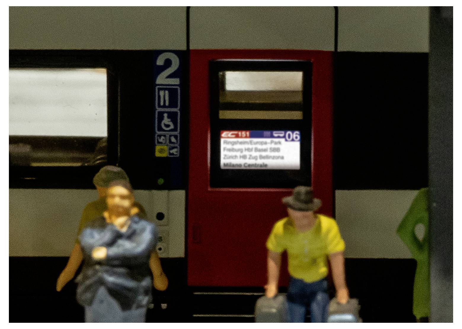 Zug mit Passagieren beim Einsteigen. Anzeigetafel zeigt IC151 nach Milano Centrale, Halt in Freiburg, Basel und Zürich. Waggon Nummer 2.