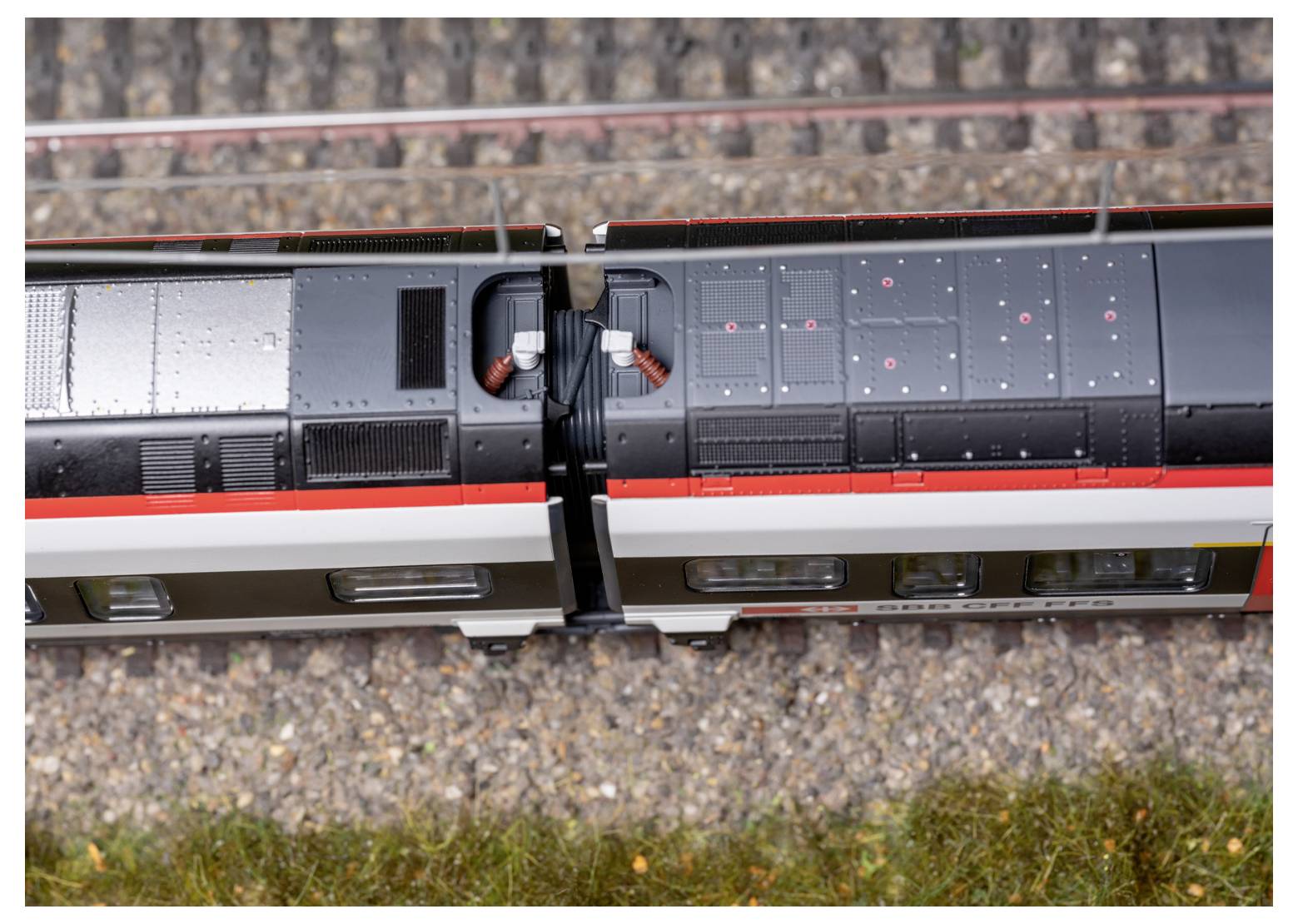 Luftaufnahme zweier verbundener Eisenbahnwaggons auf parallelen Gleisen, umgeben von industrieller und ländlicher Landschaft.