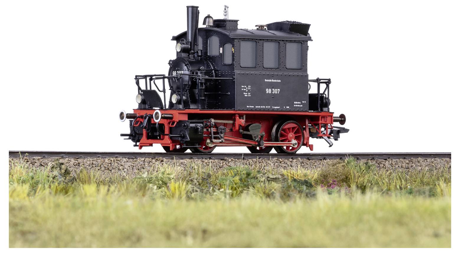 Ein Miniatur-Dampflokomotivmodell in Schwarz auf einem Gleis, von der Seite betrachtet, mit detaillierten Merkmalen und einem grasigen Vordergrund.