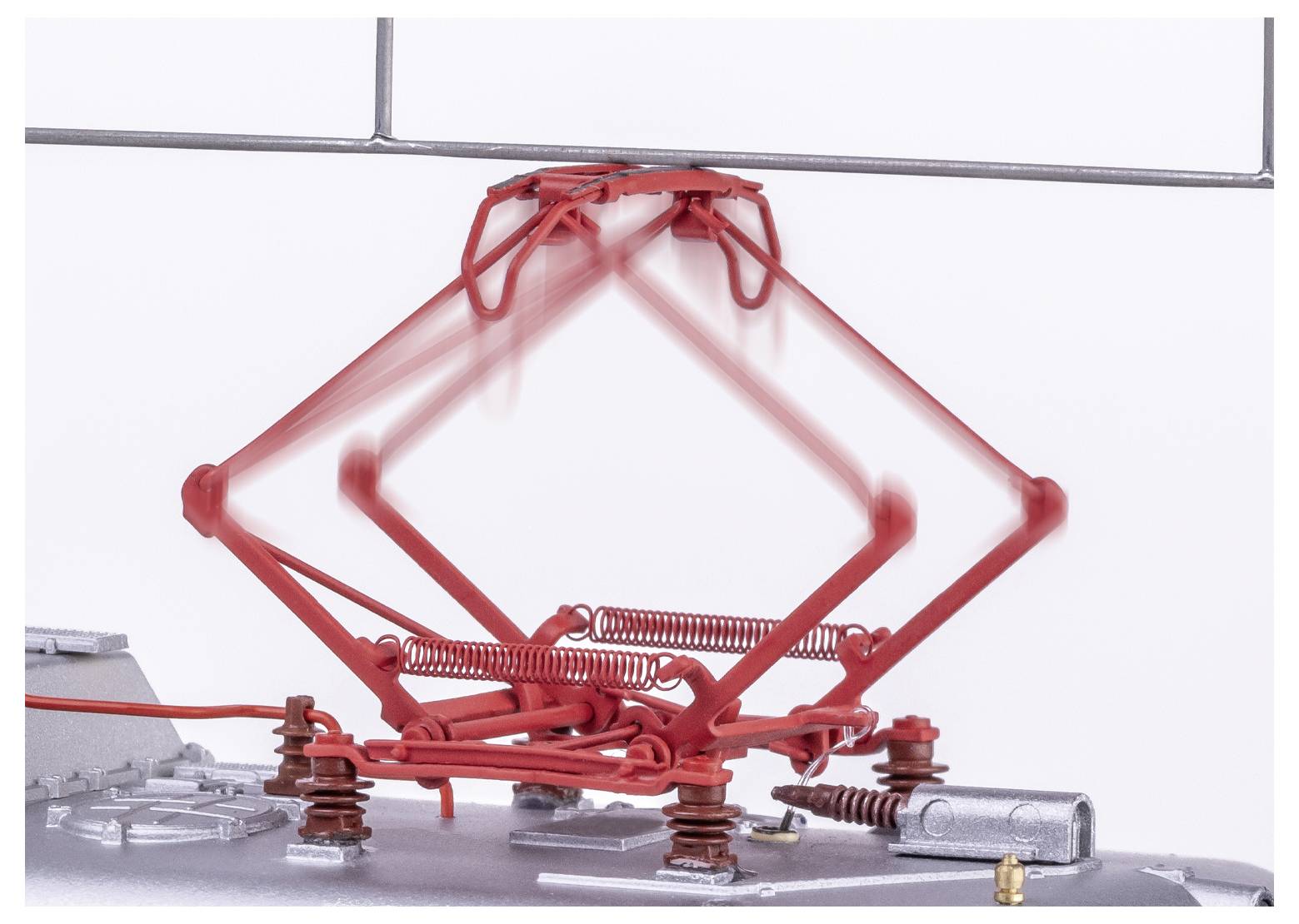Ein roter Pantograph auf dem Dach eines Zuges, nach oben ausgefahren und mit einer Oberleitung verbunden, der in einem stillstehenden Bild Bewegungsunschärfe zeigt.