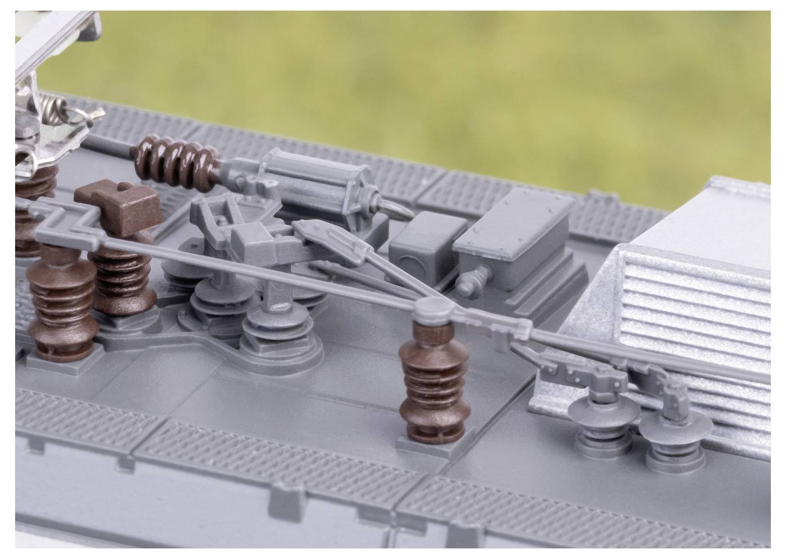 Detailaufnahme eines Modellzugdachs, die komplexe Details wie Kabel, Isolatoren und mechanische Komponenten zeigt, vor einem unscharfen Hintergrund.