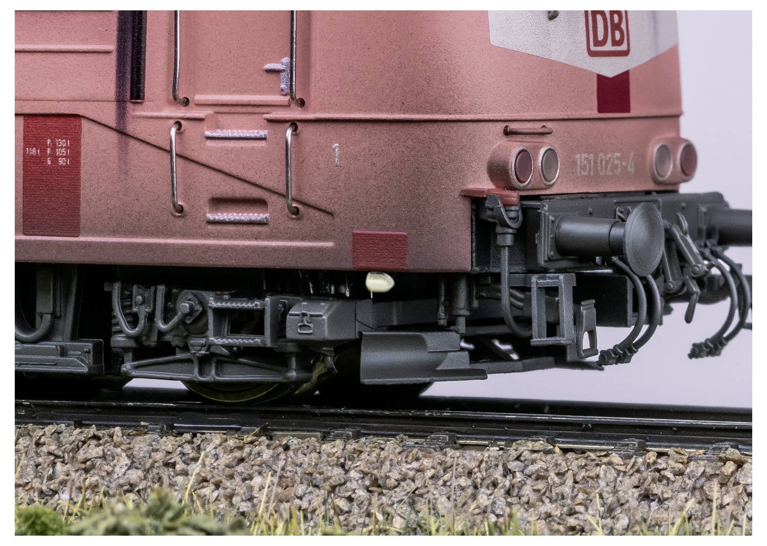 Eine Modelleisenbahn-Lokomotive, beeindruckend detailliert, von der Seite auf einem Gleis mit Kies und Grünpflanzen gezeigt, die akribische Handwerkskunst demonstriert.