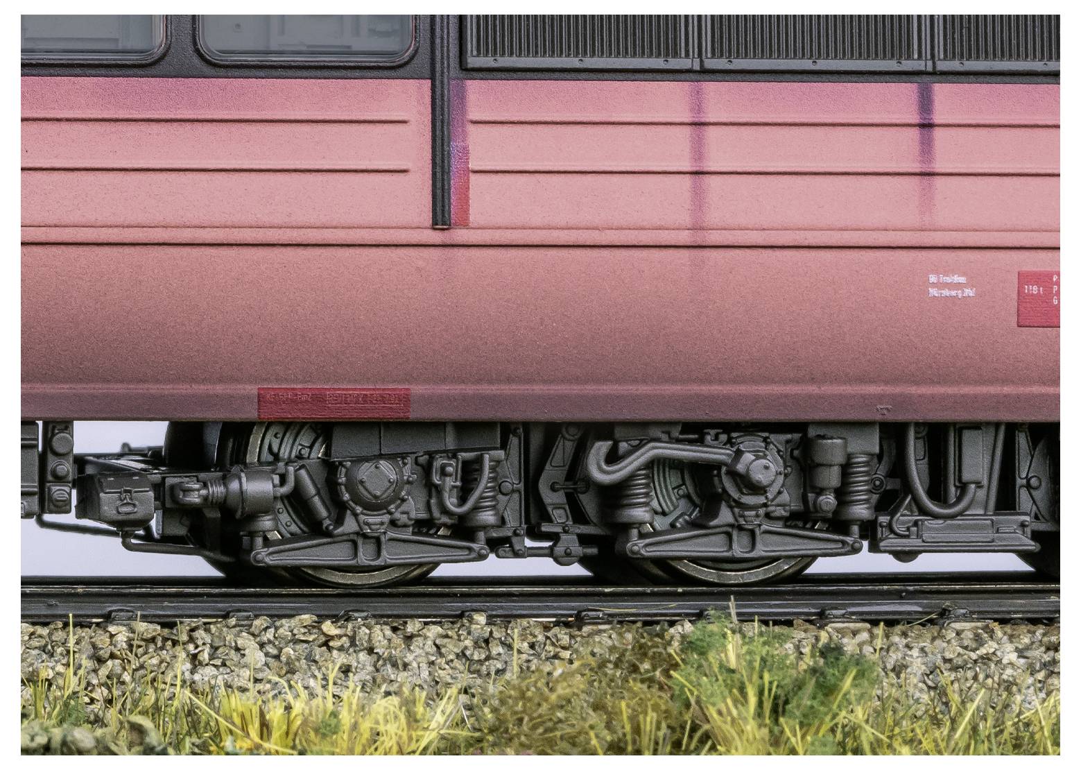 Ein Nahaufnahme der Unterseite eines Zuges, die Räder, Achsen und einen Teil des Gleises zeigt, wobei die detaillierten Mechanismen und Texturen hervorgehoben werden.