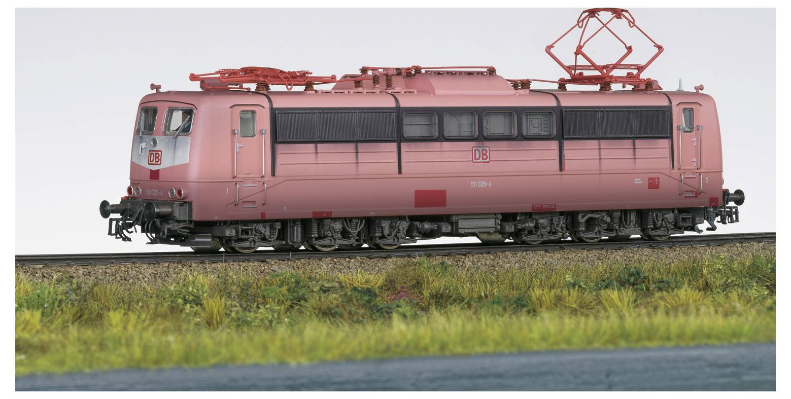 Ein rosa elektrischer Zug auf einem Gleis mit grasbewachsener Umgebung und klarem Himmel, der seine Seitenansicht und Oberleitung zeigt.
