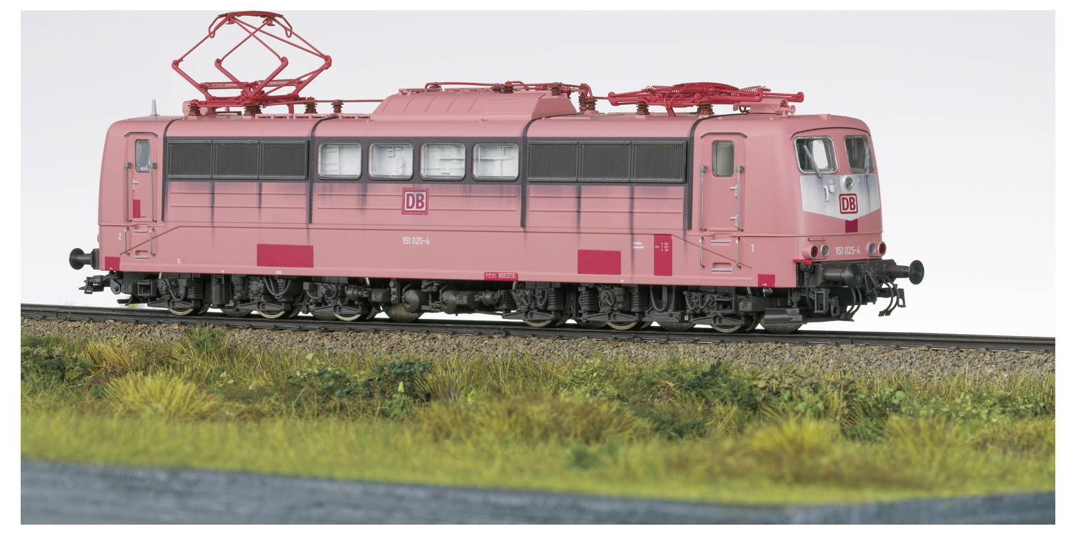 Eine rosa Modelleisenbahn-Lokomotive, die auf Schienen durch eine grüne Landschaft fährt. Die Lokomotive hat ein rotes Emblem mit weißer Schrift an der Seite.