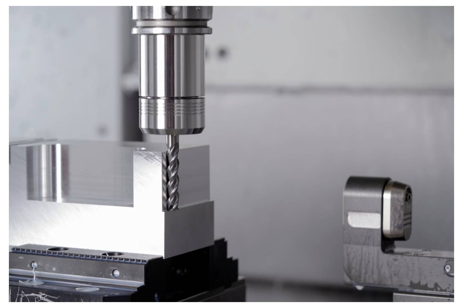 Eine Nahaufnahme einer CNC-Fräsmaschine, die in einen rechteckigen Metallblock bohrt. Das präzise Werkzeug der Maschine ist sichtbar und unterstreicht die industrielle Fertigung.