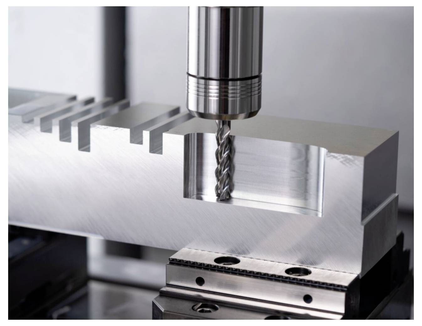 Ein Metallblock wird von einer Fräsmaschine mit einem rotierenden Bohreinsatz präzise bearbeitet und demonstriert damit Technologie der industriellen Zerspanungsfertigung.