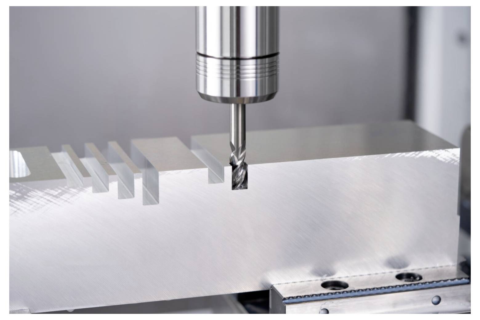 Eine metallische Fräsmaschine schneidet präzise Rillen in ein rechteckiges Metallstück und demonstriert industrielle Fertigungsprozesse.