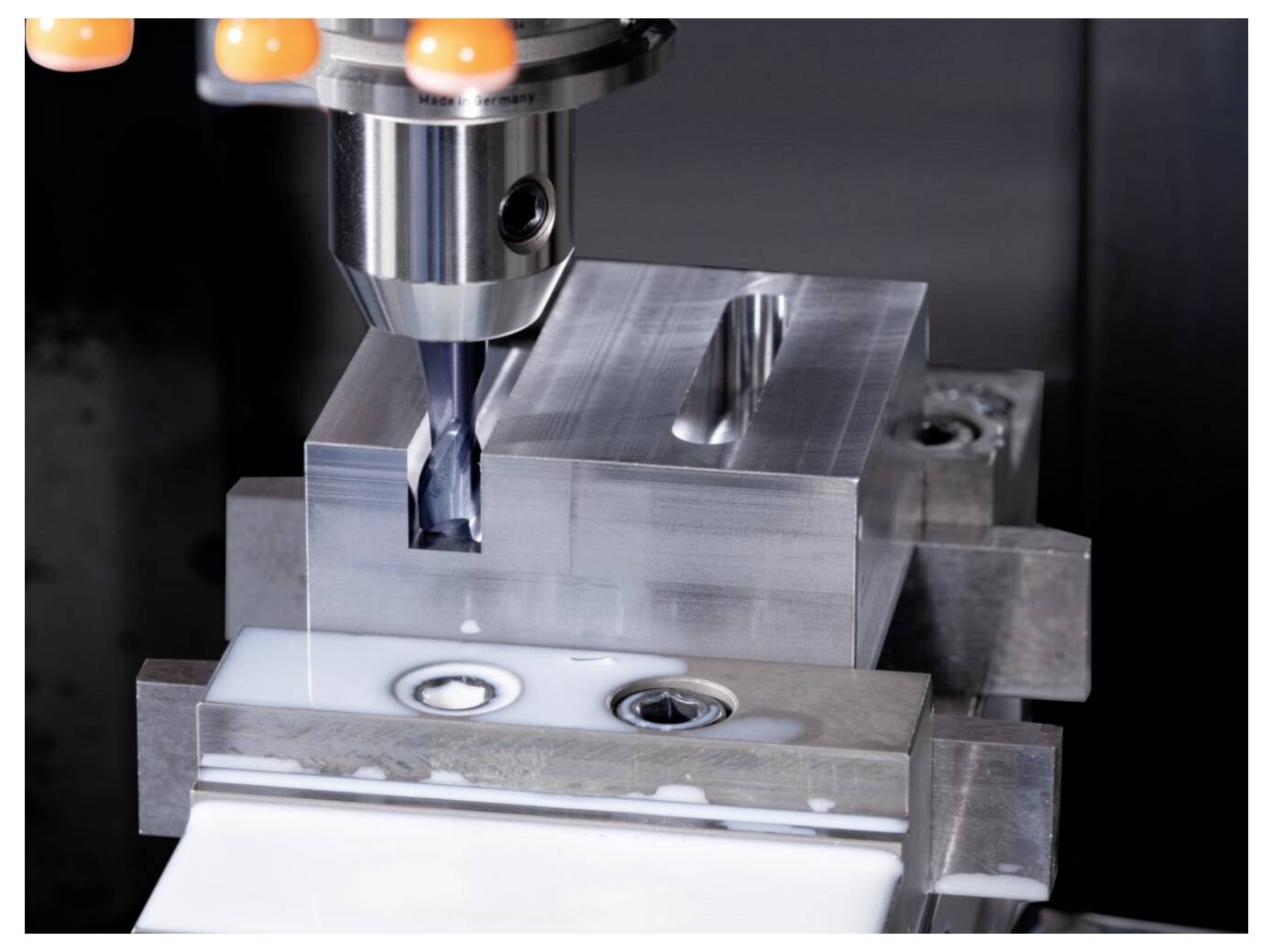 Eine Fräsmaschine, die eine präzise rechteckige Nut in einen Metallblock schneidet, mit sichtbarem Kühlmittel, die Präzisionsbearbeitung demonstrierend.