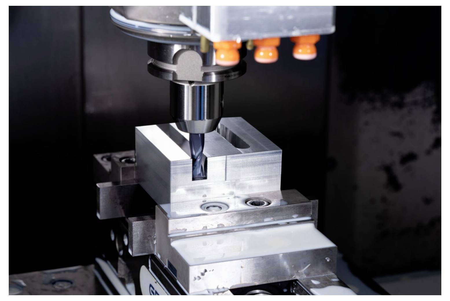 Eine CNC-Maschine bohrt einen quadratischen Metallblock präzise und veranschaulicht damit fortschrittliche Fertigungstechnologie und Präzisionsingenieurwesen.