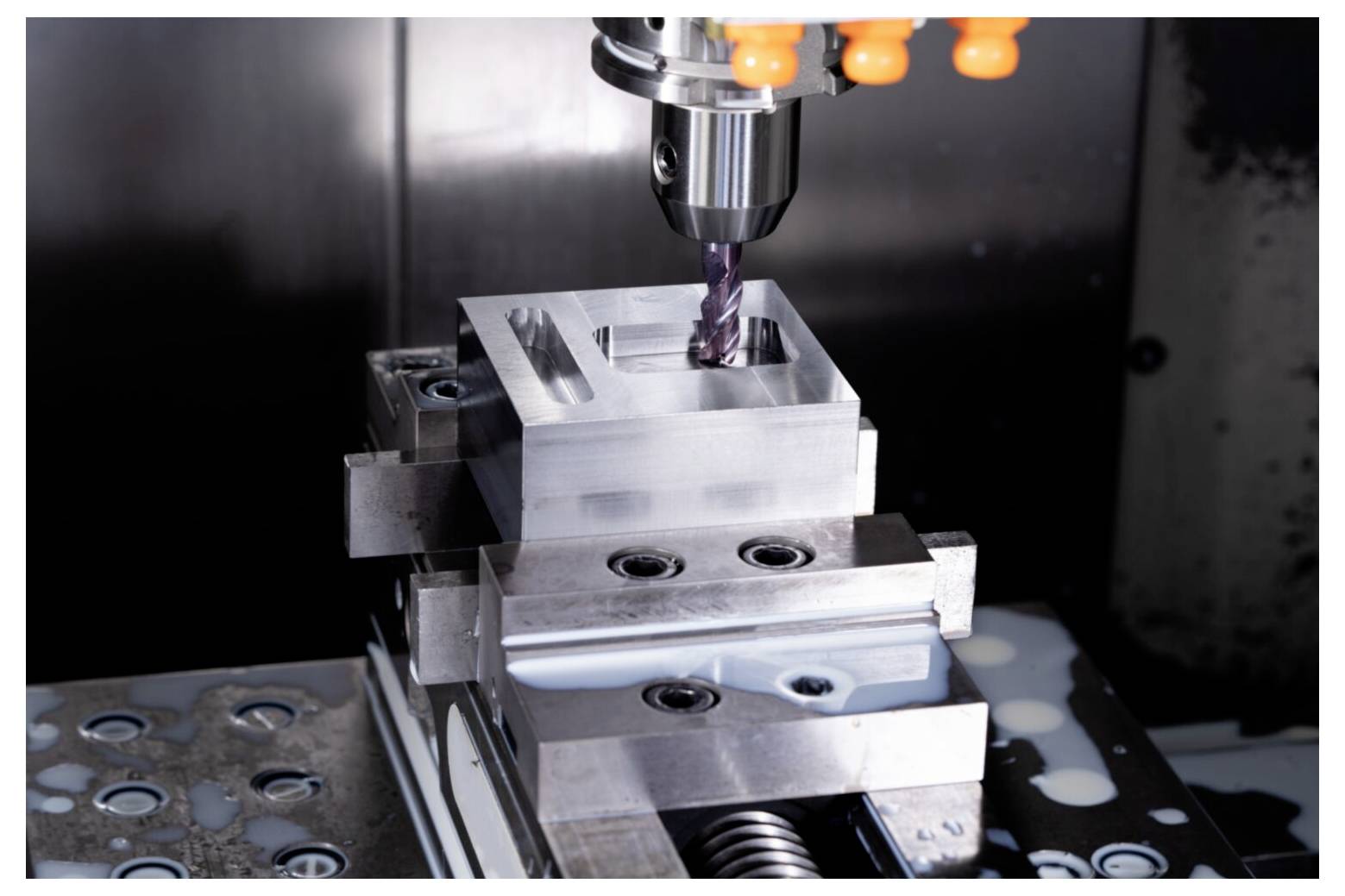 Eine CNC-Maschine bohrt präzise einen rechteckigen Metallblock. Der Block ist fest eingespannt, wobei ein Bohrer aktiv in seine Oberfläche eindringt.