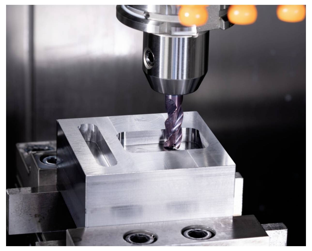 Eine Metallfräsmaschine mit einem Bohrer bearbeitet einen rechteckigen Block und demonstriert präzise Ingenieur- und Fertigungsprozesse.