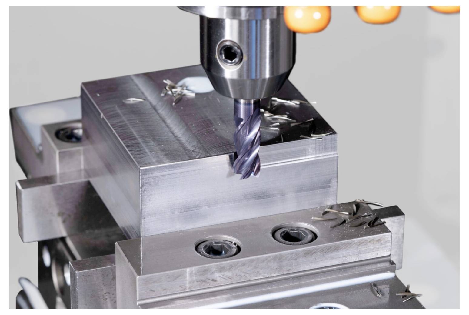 Eine CNC-Maschine fräst einen Metallblock präzise mit einem rotierenden Werkzeug und erzeugt dabei kleine Metallspäne auf der Oberfläche.