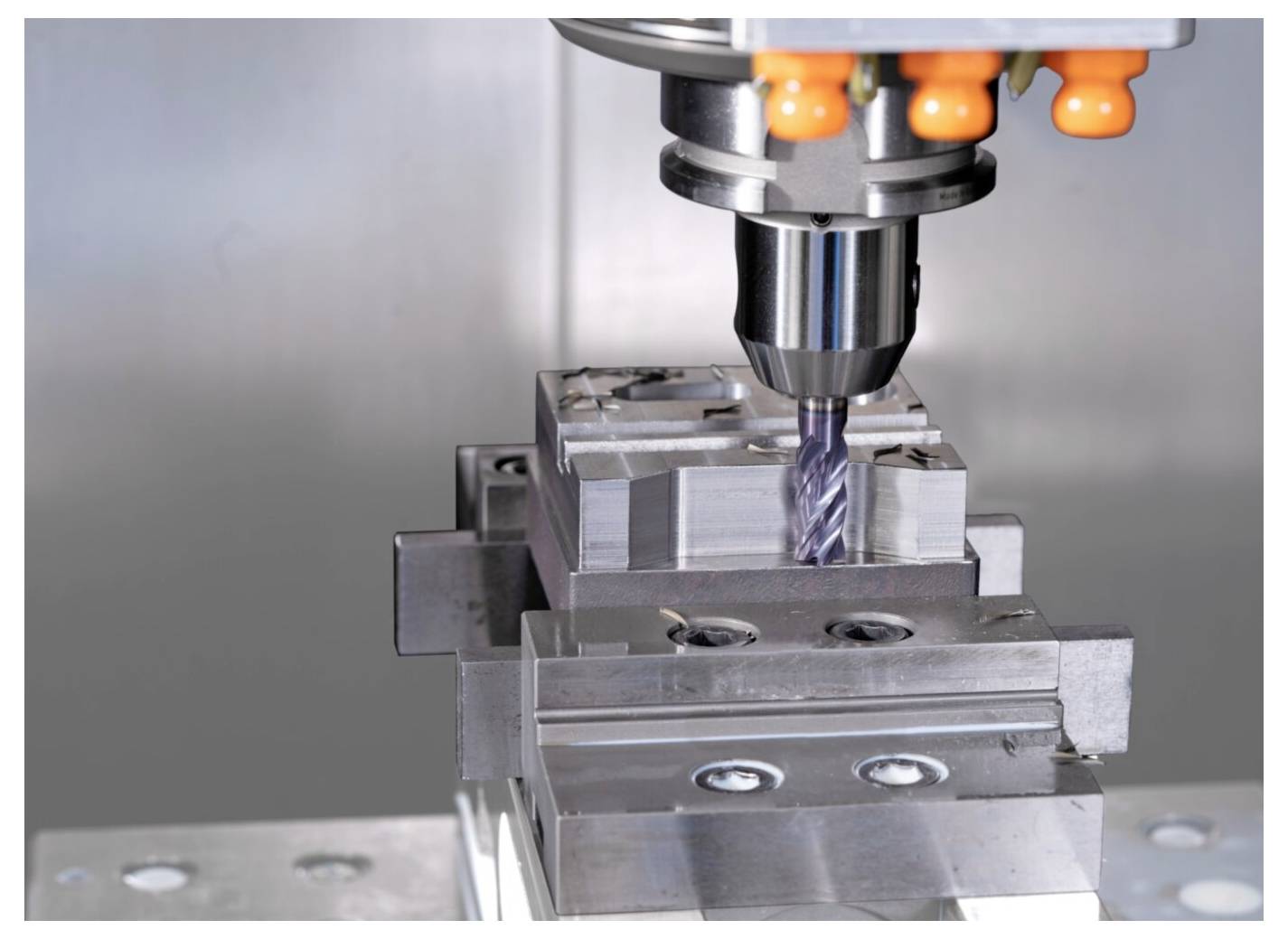 Eine CNC-Fräsmaschine, die einen Metallblock bearbeitet, mit grauen Maschinenkomponenten und einer industriellen Kulisse, die präzise Fertigungstechnik veranschaulicht.