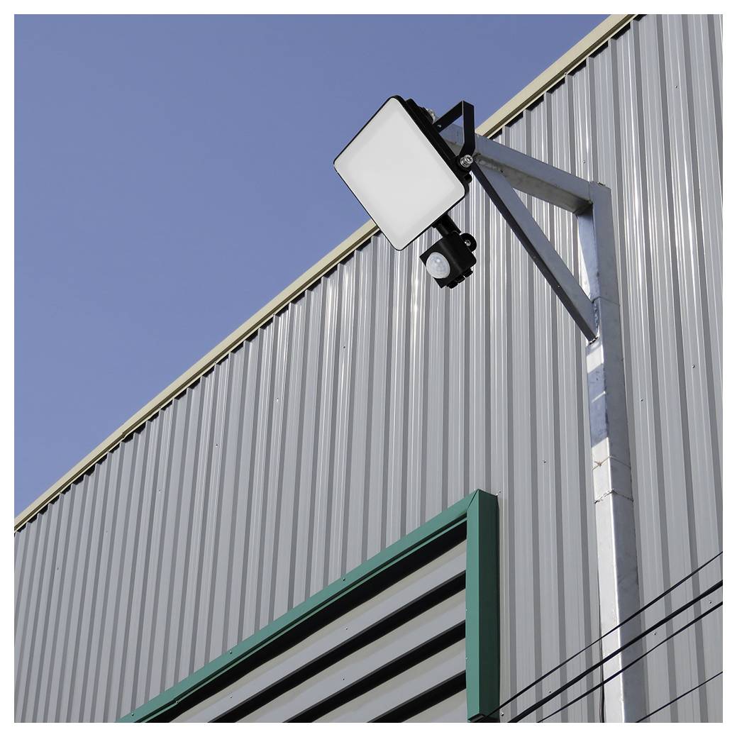 Ein Metallgebäude mit einer Flutlichtlampe und einer Sicherheitskamera, die an der Seite befestigt sind, unter einem klaren blauen Himmel.