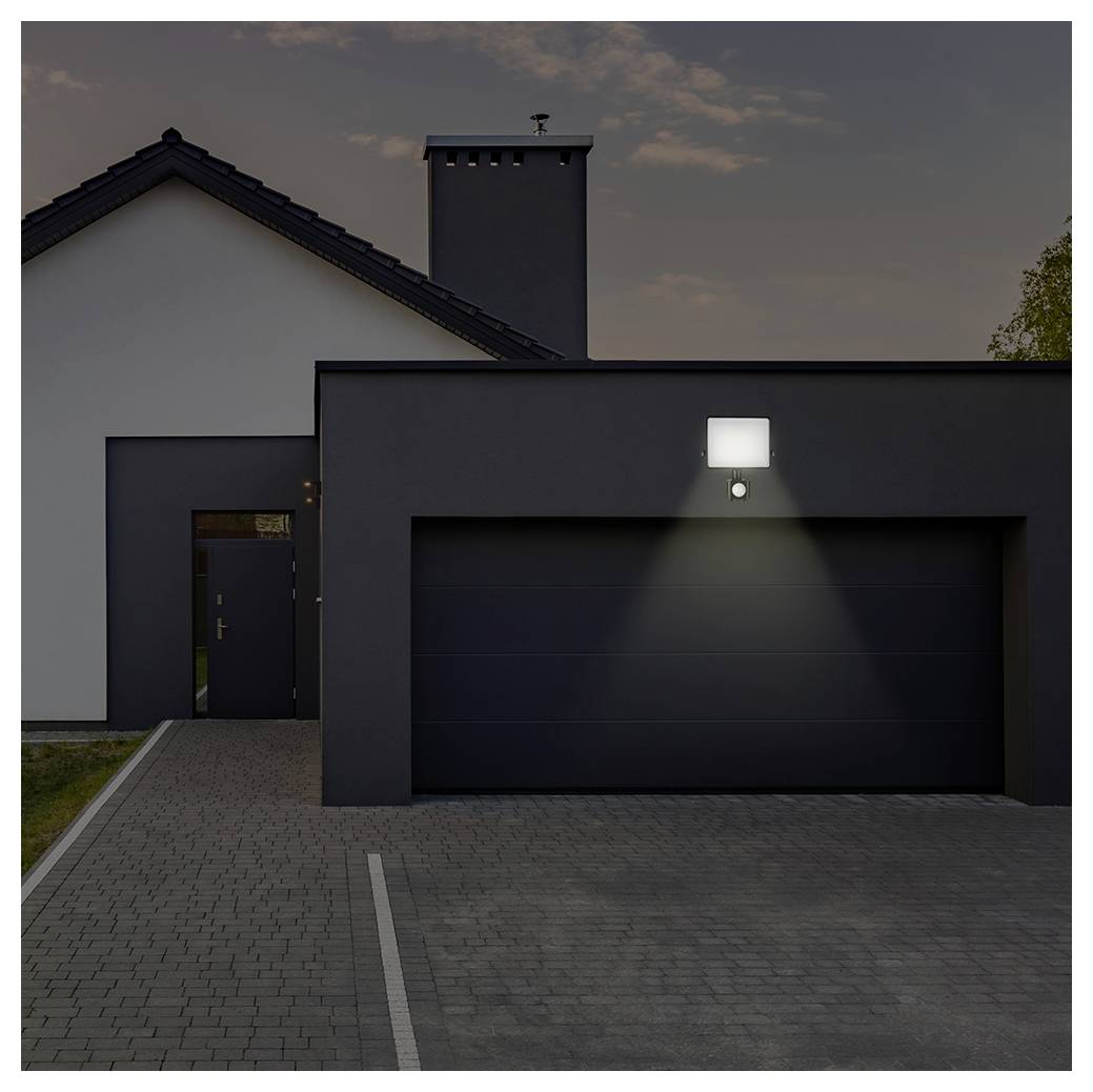 Eine moderne Hausaußenansicht in der Abenddämmerung, bei der ein bewegungssensorisches Licht die Auffahrt vor einem geschlossenen Garagentor beleuchtet.