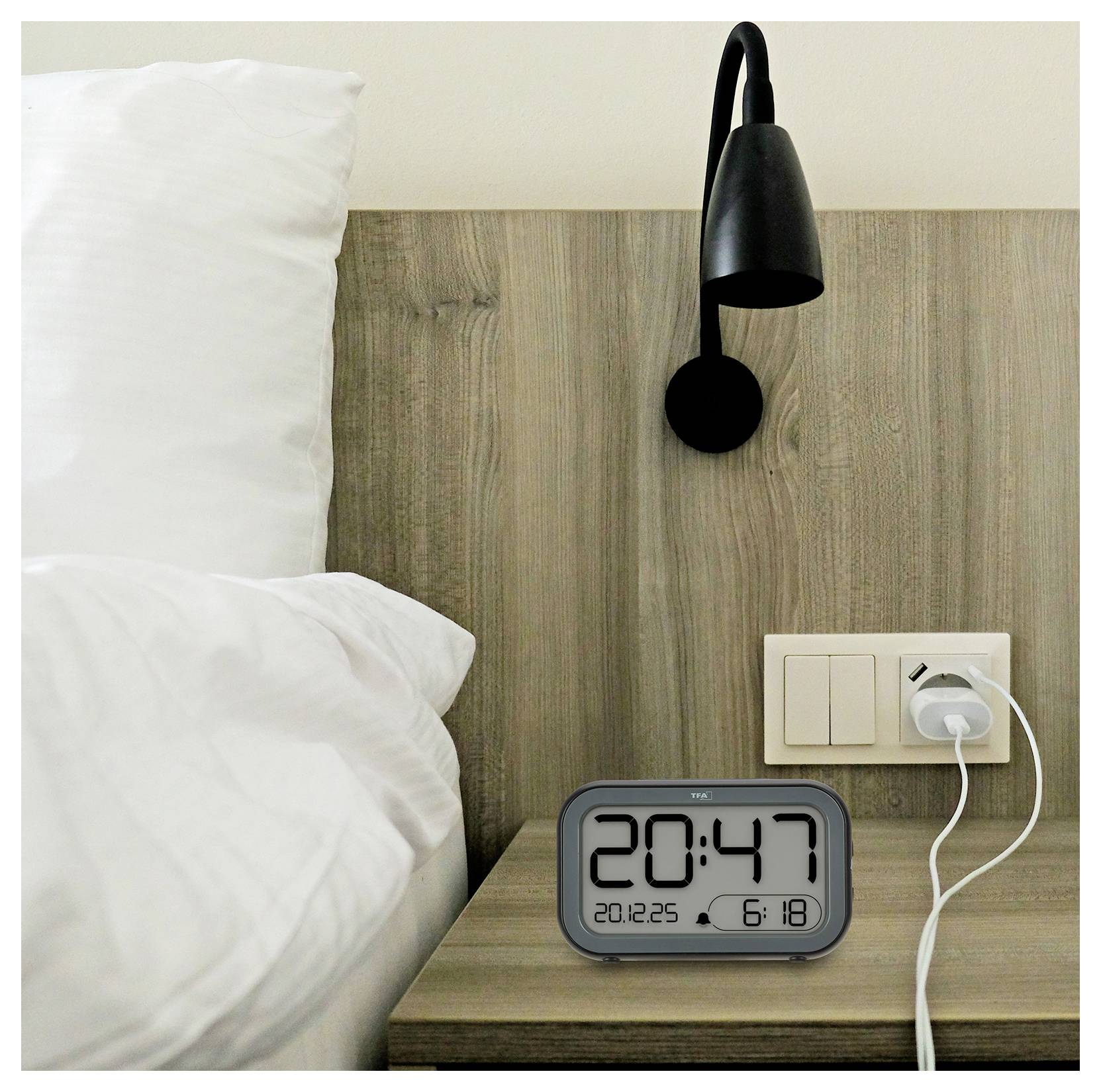 Eine digitale Uhr auf einem Holznachttisch zeigt '20:47'. Ein Bett, eine Wandlampe und ein ladendes Telefon befinden sich im Hintergrund und deuten auf eine gemütliche Schlafzimmerszene hin.