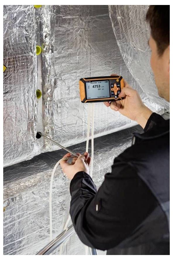 Eine Person, die ein tragbares Gerät verwendet, um die Luftqualität in einem Kanal mit reflektierender Isolierung zu messen. Das Gerät zeigt eine Messung von '4753' an.