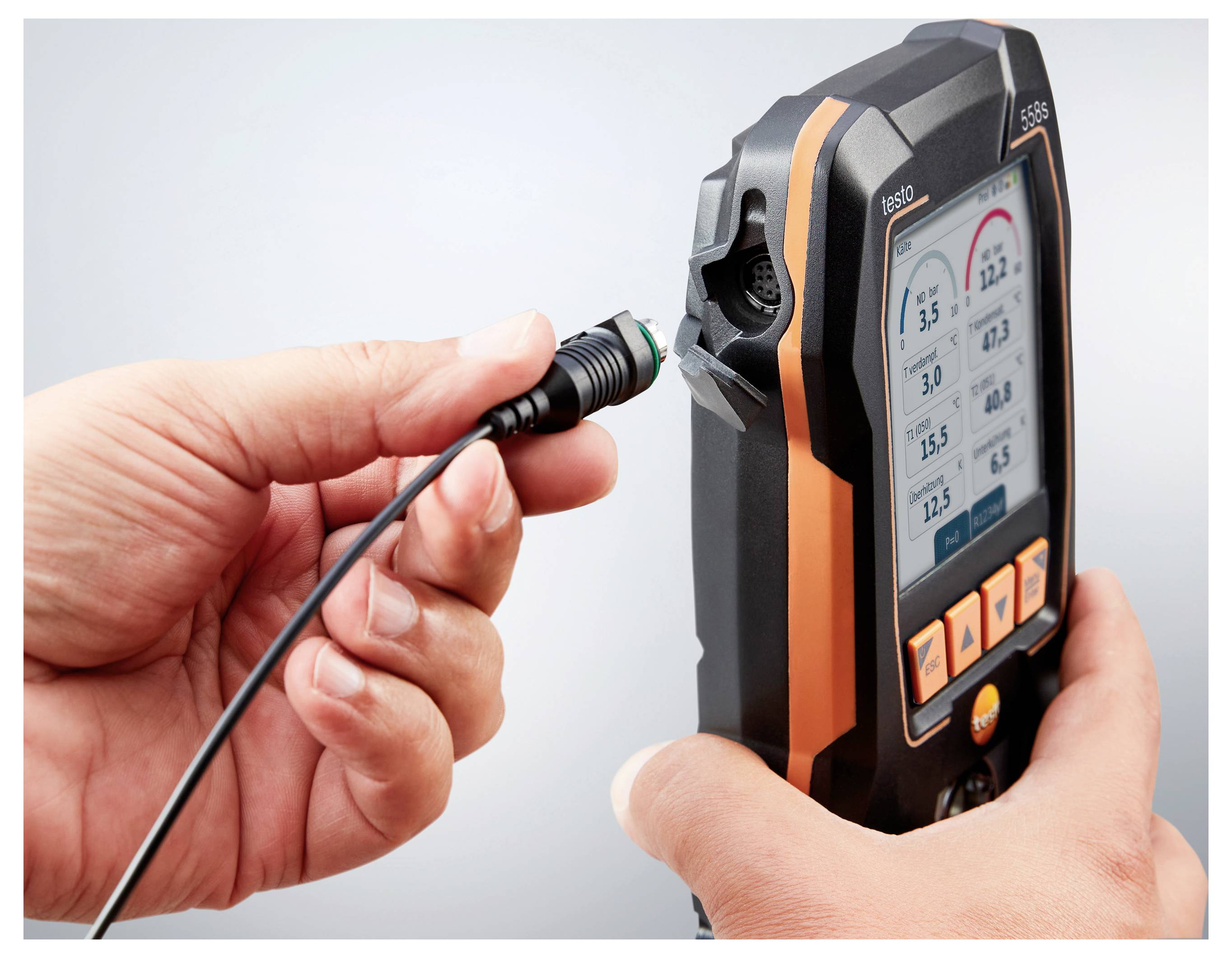 Eine Person schließt ein Kabel an ein orange-schwarzes Gerät an, das Messdaten auf seinem Bildschirm anzeigt und für Tests oder Diagnosen verwendet wird.