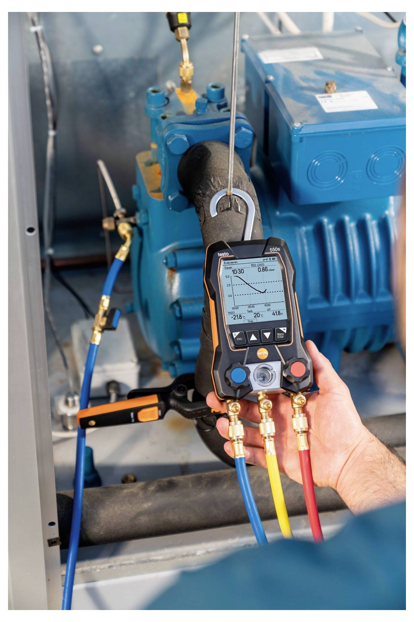 Eine Person hält ein digitales Messgerät an einer blauen Industriemaschine und prüft vermutlich Druck- oder Leistungsindikatoren.