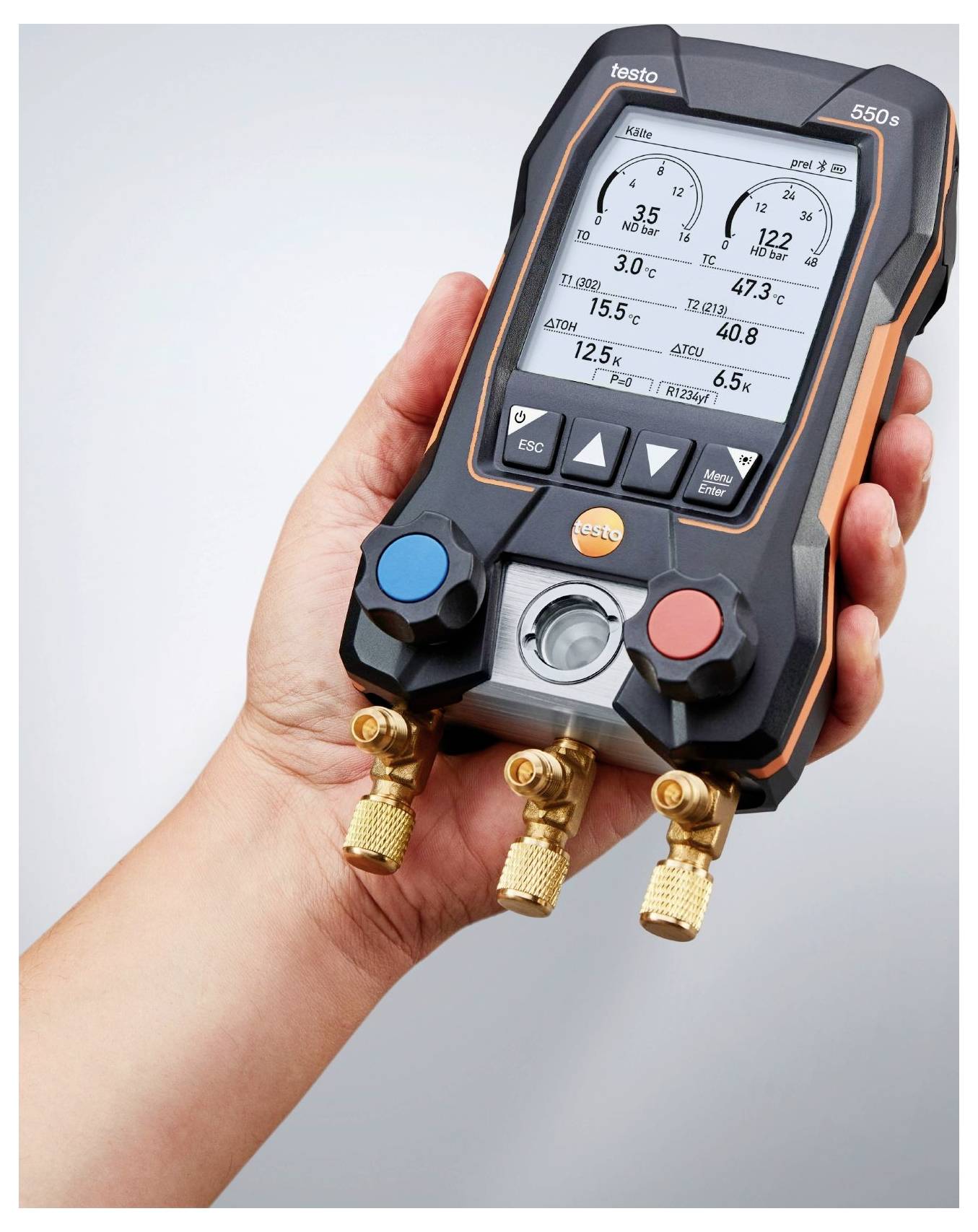 Eine Hand hält ein digitales HVAC-Messgerät, das Druck- und Temperaturmessungen anzeigt, mit drei Messingverbindern am unteren Rand.