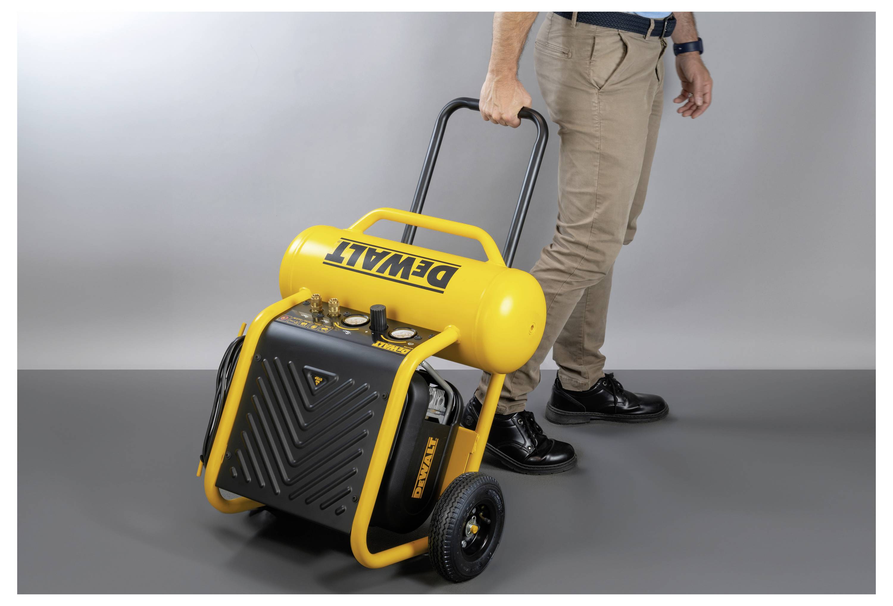 Eine Person zieht einen gelben tragbaren Luftkompressor an einem Griff. Der Markenname ist auf dem Tank sichtbar. Das Gerät verfügt über Räder für einfache Bewegung.