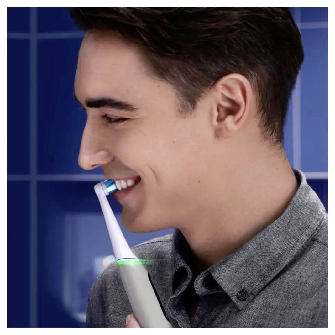 Eine Person im Profil lächelt, während sie eine elektrische Zahnbürste an ihre Zähne hält und damit die Verwendung der Mundhygiene demonstriert.