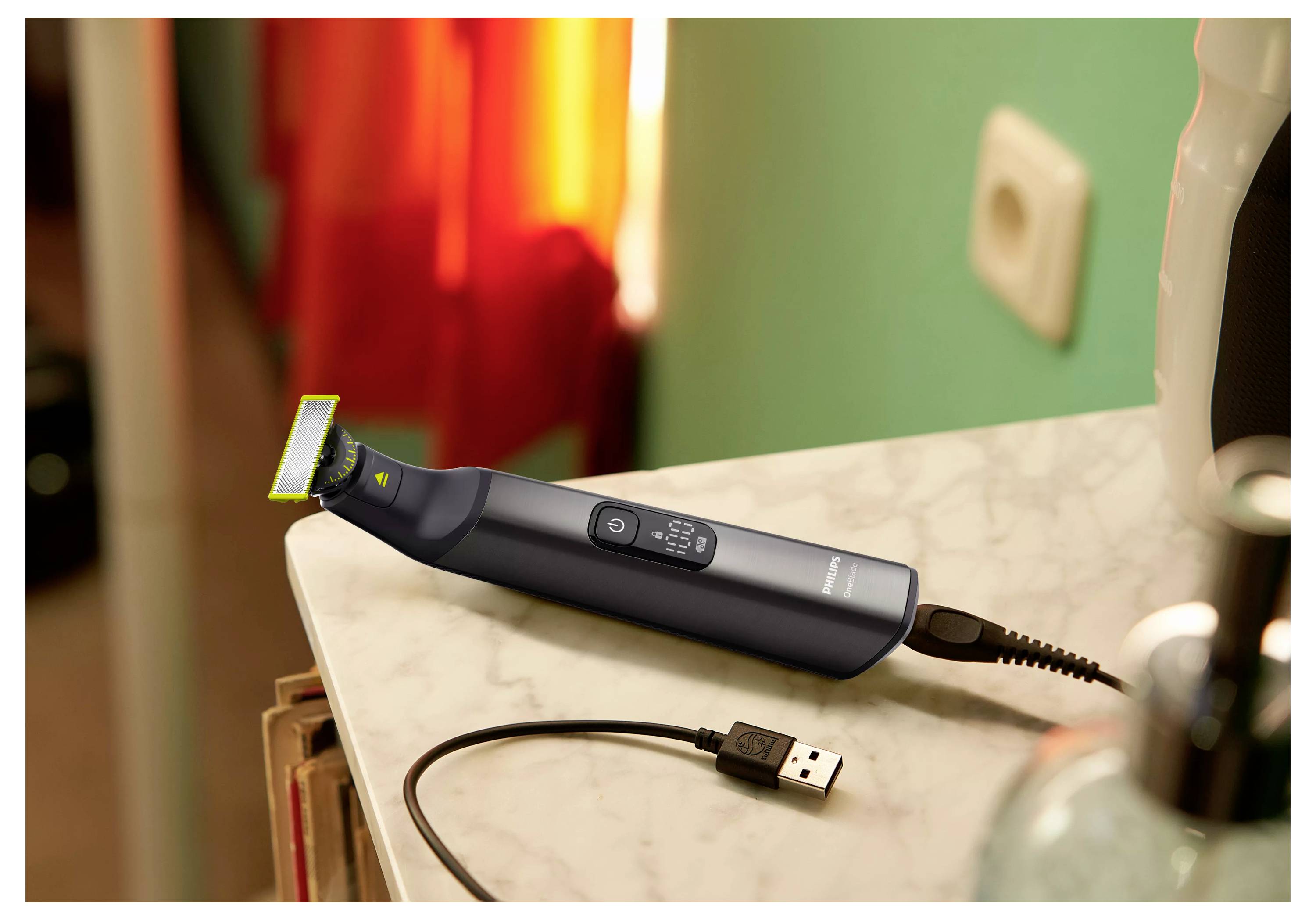 Ein schwarzer und limegrüner elektrischer Trimmer, der auf einer Marmorarbeitsplatte liegt, mit einem USB-Ladekabel verbunden, vor einem unscharfen Raumhintergrund.