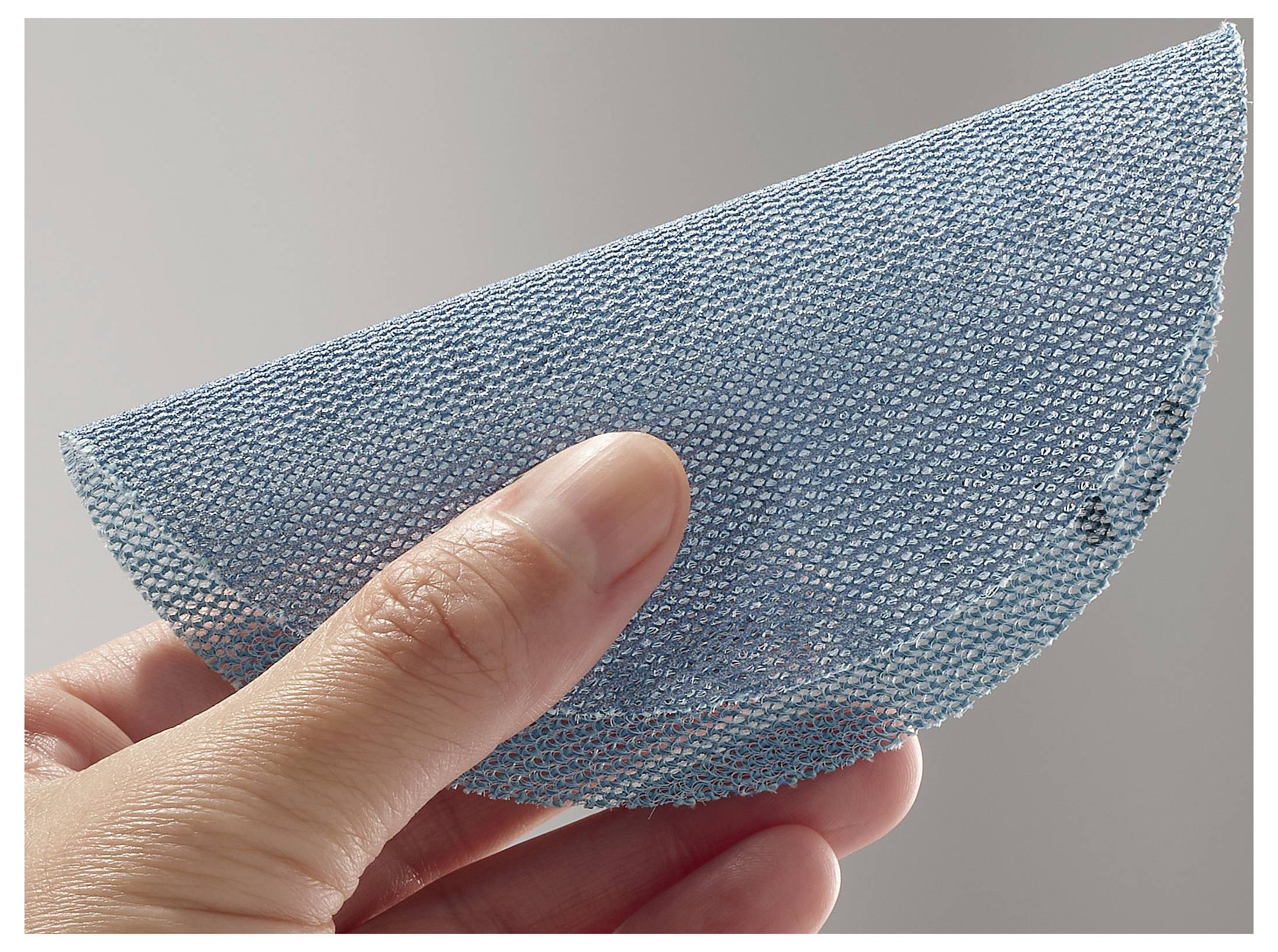 Eine Hand hält ein halbkreisförmiges Stück blaues Netzstoffgewebe vor einem einfarbigen Hintergrund, wodurch seine Textur und flexible Beschaffenheit hervorgehoben werden.