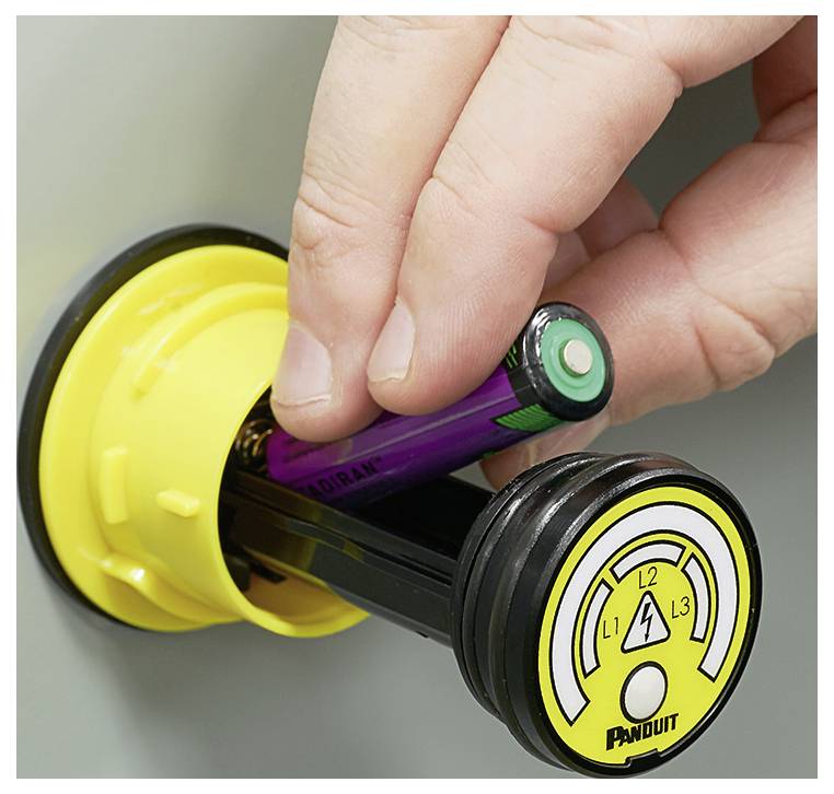 Eine Hand befestigt eine gelbe Sperrvorrichtung an einem elektrischen Schalter mit einem violetten Zylinder, der mit 'LOKSAFE' gekennzeichnet ist, um die Sicherheitsvorschriften einzuhalten.