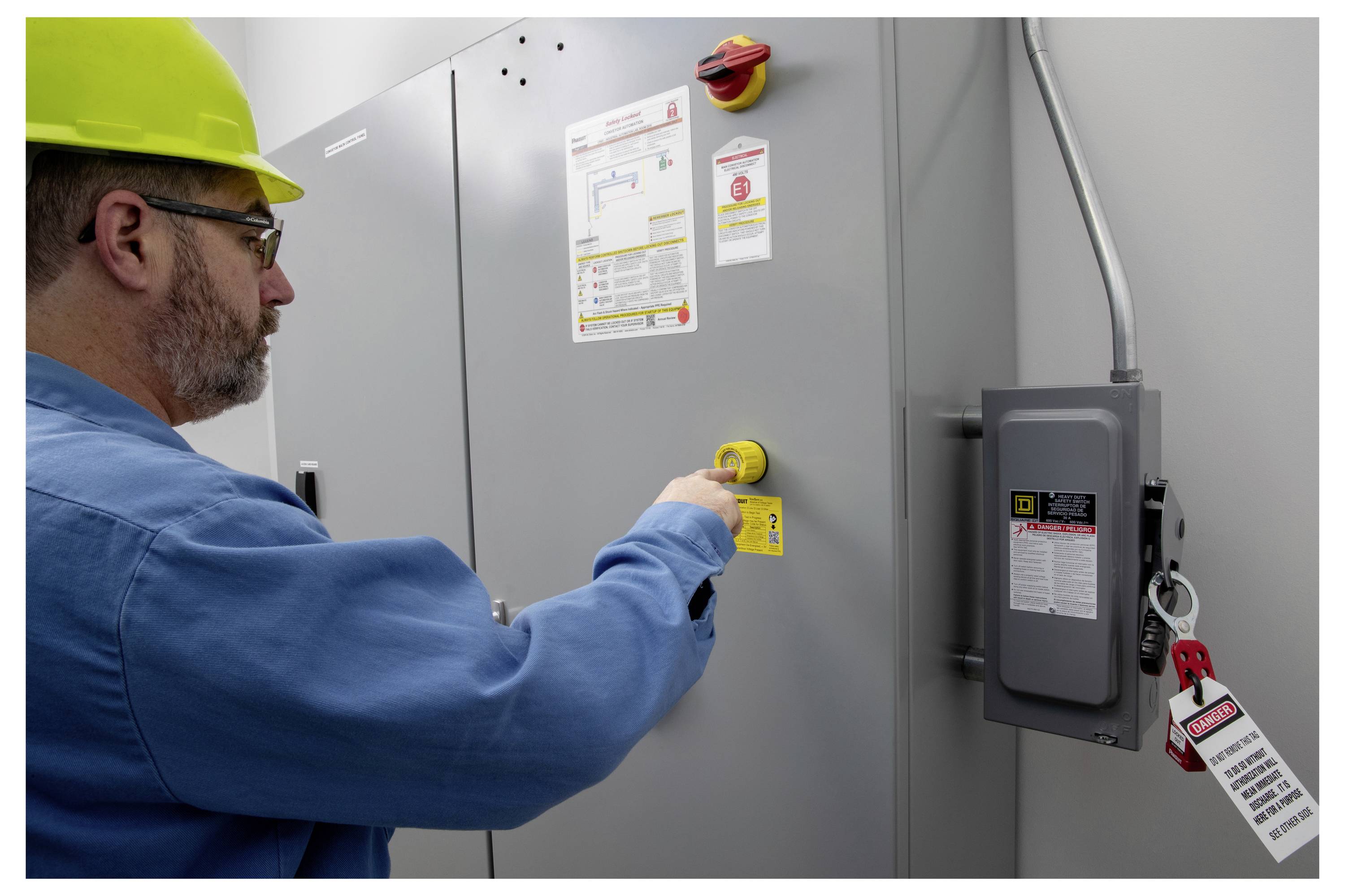 Eine Person mit Schutzhelm und Schutzbrille drückt einen Notaus-Knopf an einem großen industriellen Kontrollpanel.