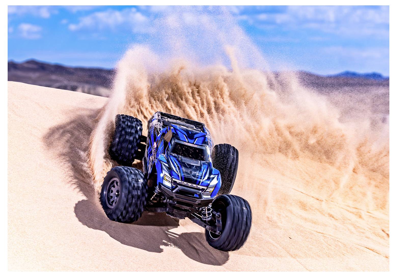 Ein ferngesteuerter Truck wirbelt Sand auf, während er einen Wüstenhügel hinunterrast unter einem klaren blauen Himmel.