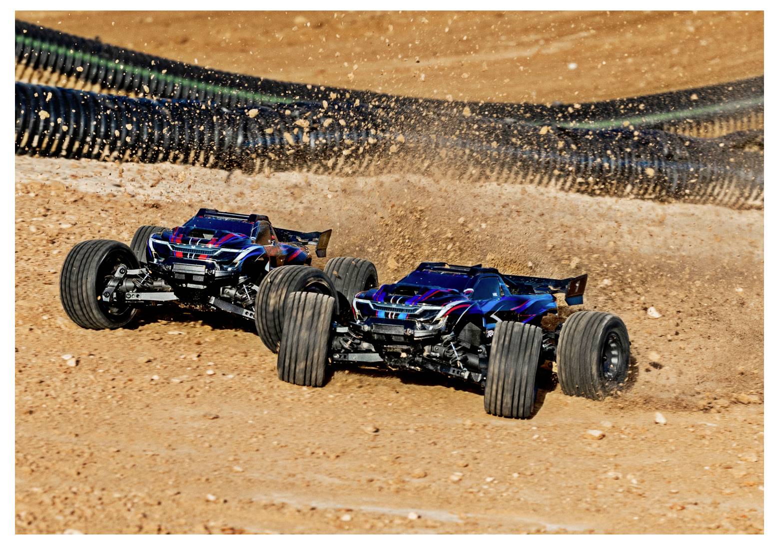 Zwei ferngesteuerte Autos rasen auf einer Schotterpiste, wirbeln Staub auf, während sie eine Kurve nehmen und Geschwindigkeit und Wendigkeit demonstrieren.