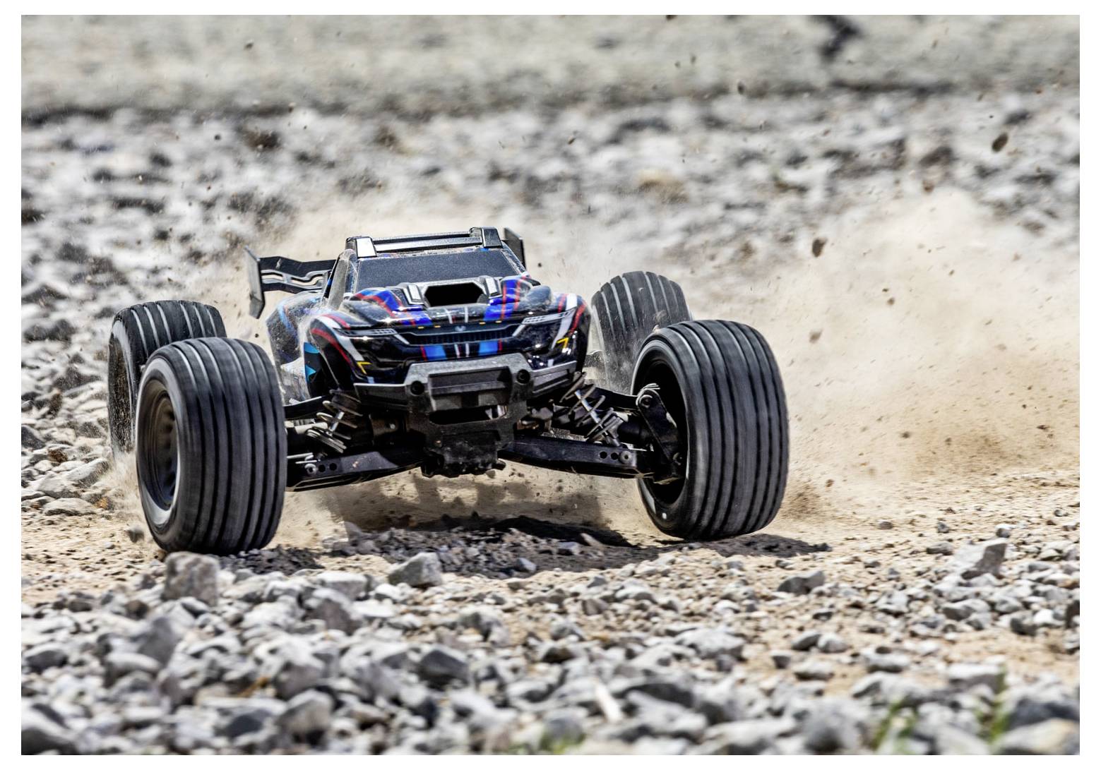 Ein ferngesteuertes Auto bewegt sich schnell über ein felsiges Gelände und wirbelt dabei Staub auf. Das Auto verfügt über große Räder und ein schlankes Design.