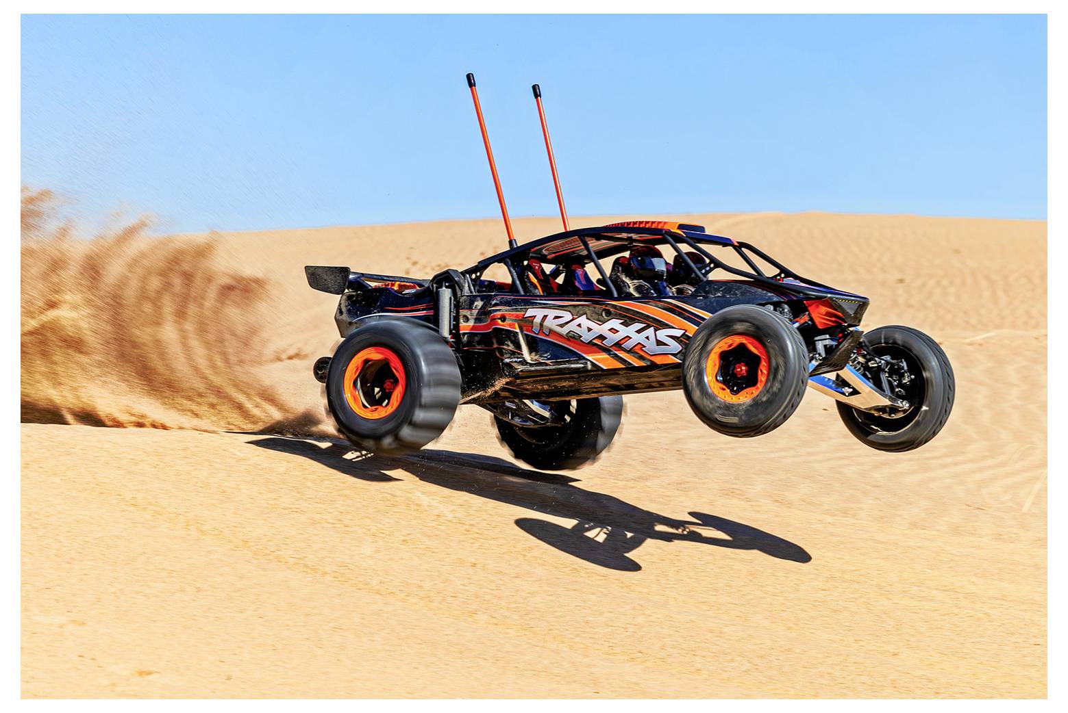 Ein ferngesteuertes Auto mit orange-schwarzem Design rast über Sanddünen und hinterlässt eine Staubspur vor einem klaren blauen Himmel.