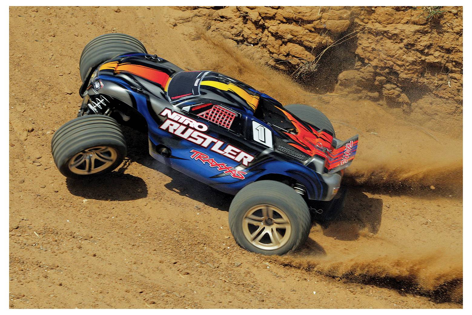 Ein ferngesteuertes Auto in leuchtenden Farben rast durch den Schmutz und wirbelt dabei Staub auf, was hohe Geschwindigkeit und Beweglichkeit auf unebenem Gelände andeutet.