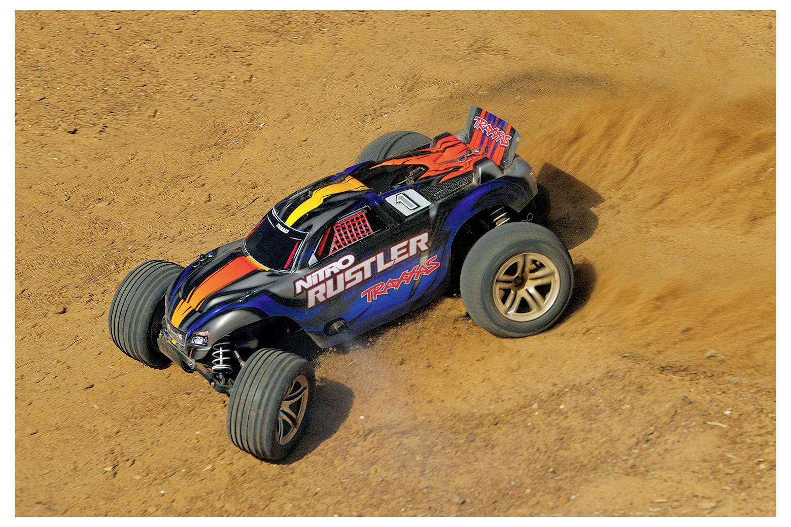Ein ferngesteuertes Auto mit der Aufschrift 'Nitro Rustler Traxxas', mit sportlichem Design, das auf einer Schotterpiste fährt und bei einer Kurve Staub aufwirbelt.