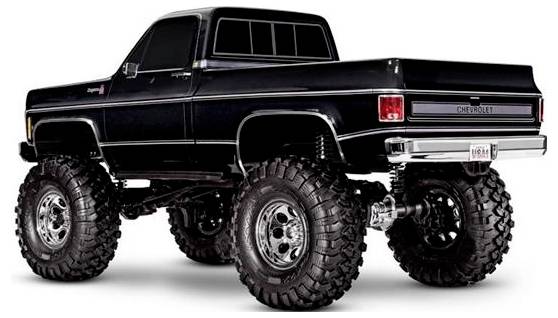 Ein angehobener Vintage-Schwarzer Pickup-Truck mit übergroßen Reifen, Chromfelgen und einem Chevrolet-Logo auf der Rückseite, von der hinteren Ecke aus betrachtet.