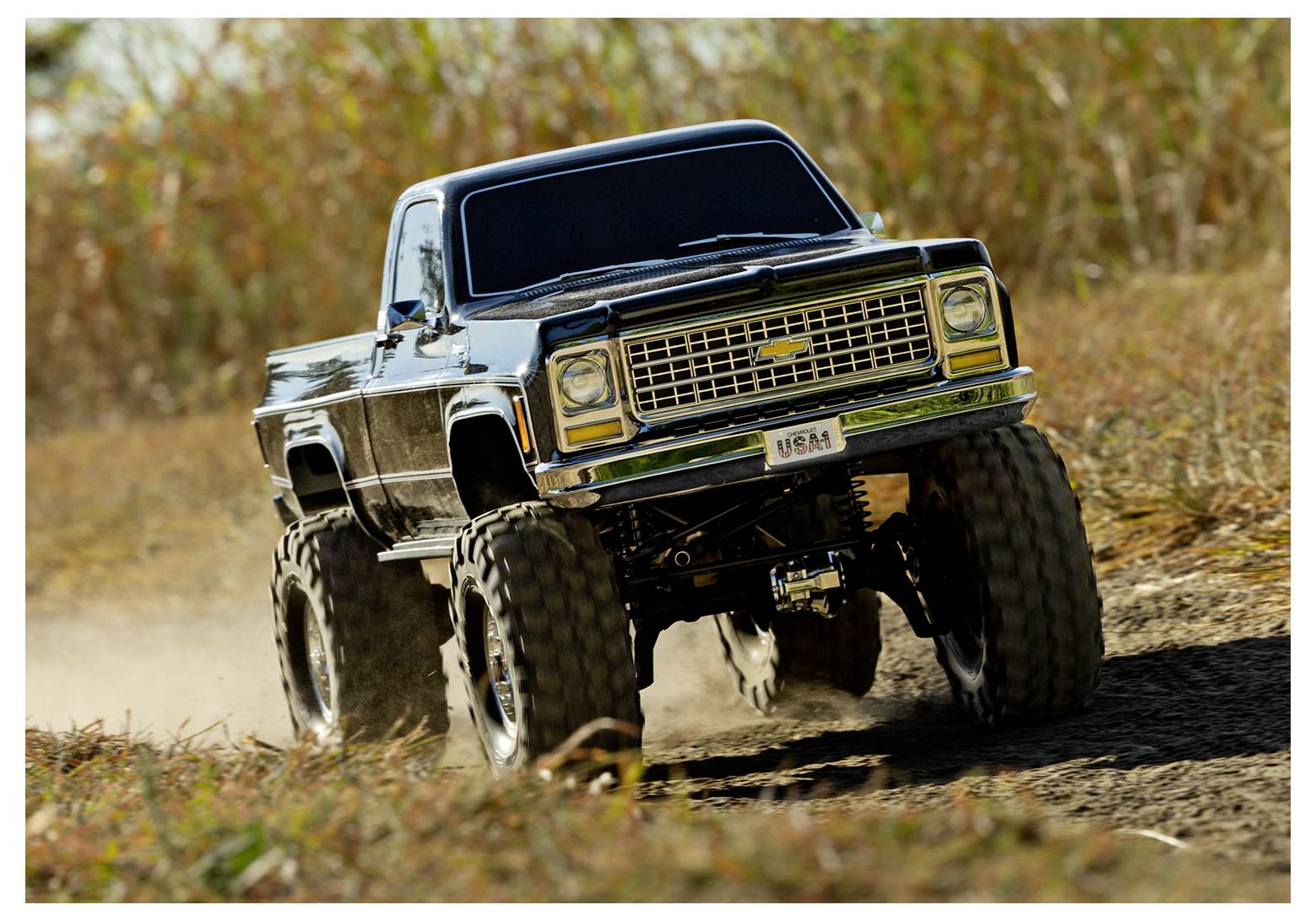 Ein angehobener Geländewagen mit großen Reifen fährt auf einem Schotterpfad, umgeben von grünem Gras, was eine Outdoor-Abenteuer-Szenerie andeutet.