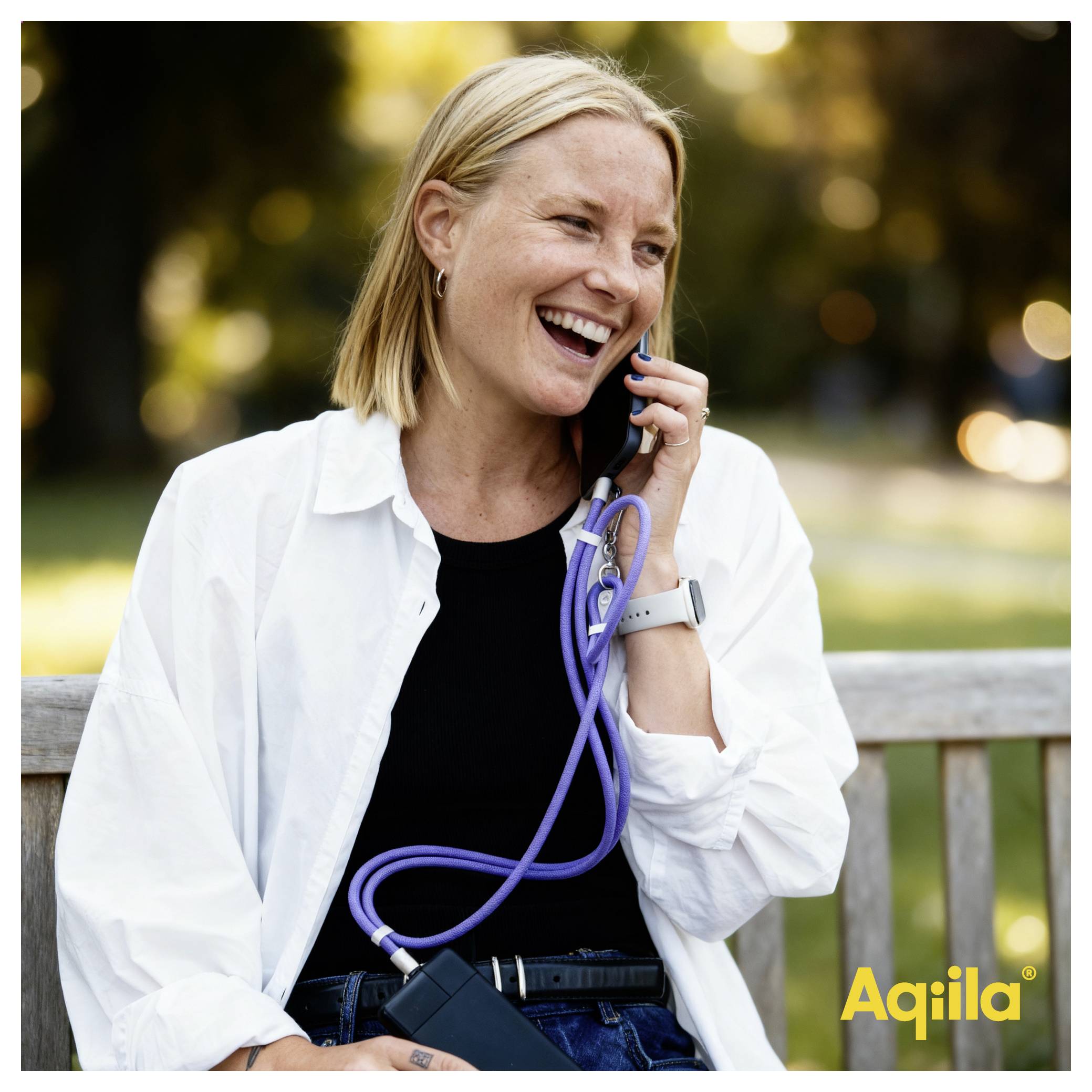 Eine Frau auf einer Parkbank lächelt, während sie ein Stethoskop und ein Smartphone hält und engagiert wirkt. Das Wort 