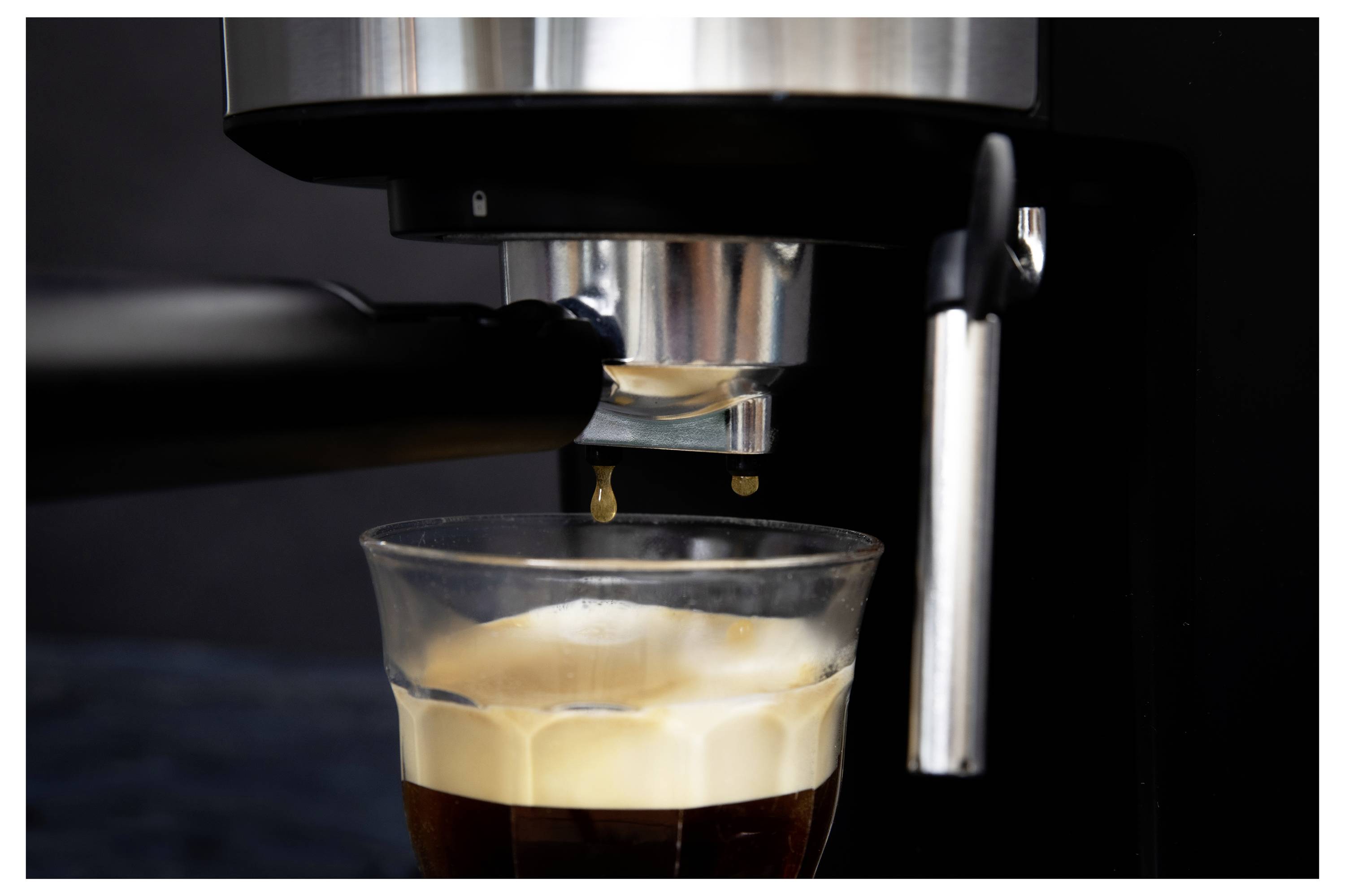 Espressomaschine, die einen Espresso in ein durchsichtiges Glas einschenkt, wobei sich eine Crema an der Oberfläche bildet.