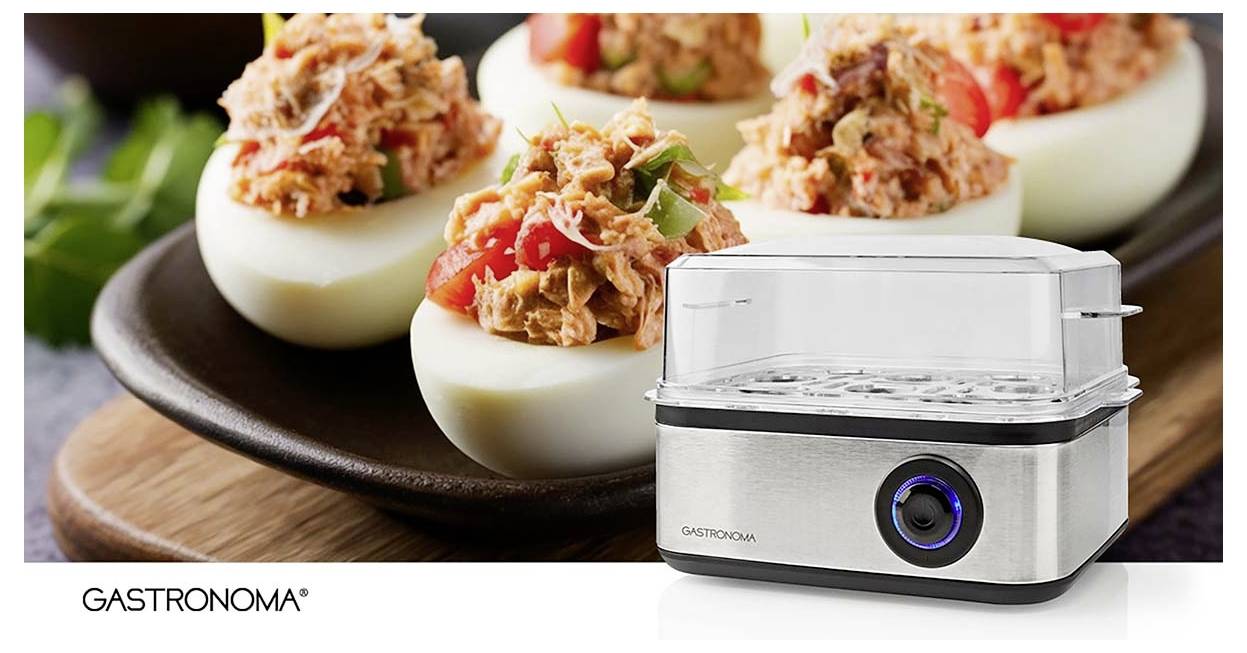 Elektrischer Eierkocher der Marke 'Gastronoma' im Vordergrund; Platte mit Deviled Eggs und Garnitur im Hintergrund.