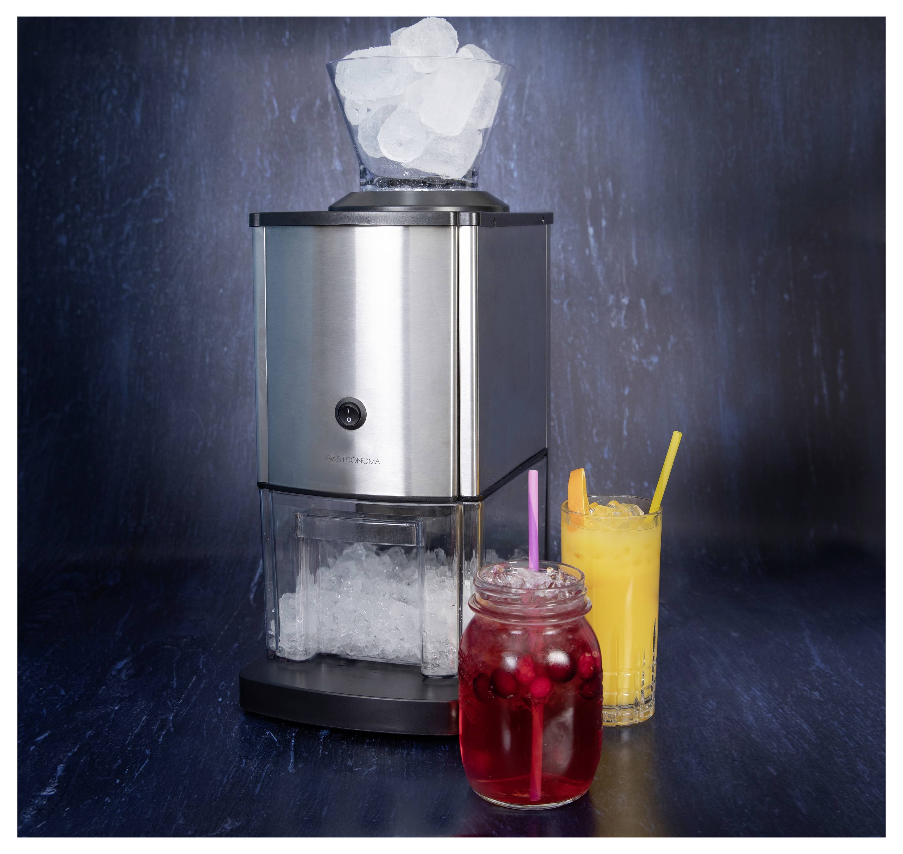 Eine silberne Eismaschine mit Eiswürfeln, die sich im oberen Schacht angesammelt haben. Davor stehen zwei Getränke: ein rotes Getränk mit Beeren und einem Strohhalm sowie ein orangefarbenes Getränk mit einer Orangenscheibe und einem Strohhalm.