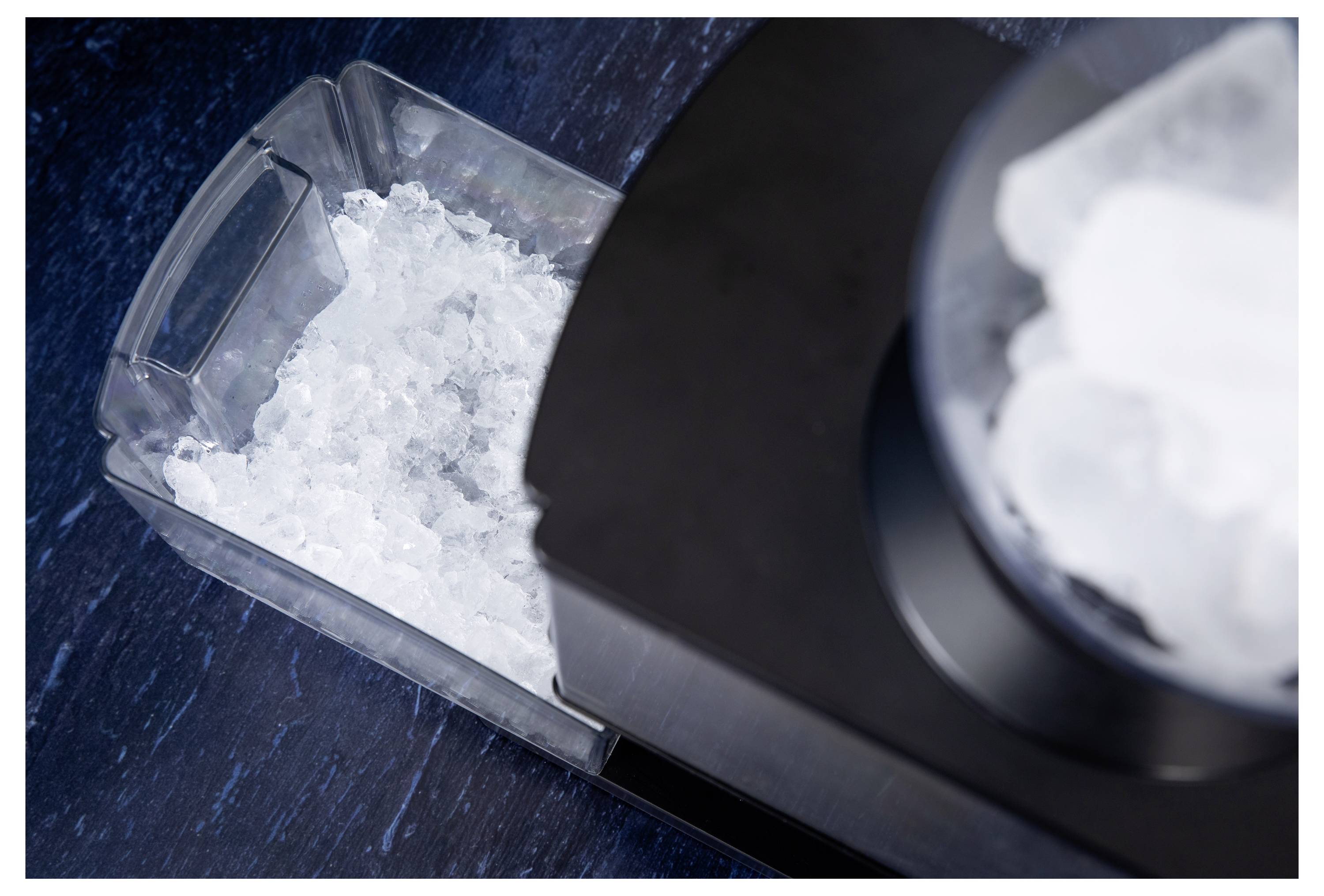 Eine Eismaschine, die Crushed Ice in einen Plastikbehälter auf einer dunklen, strukturierten Oberfläche füllt.