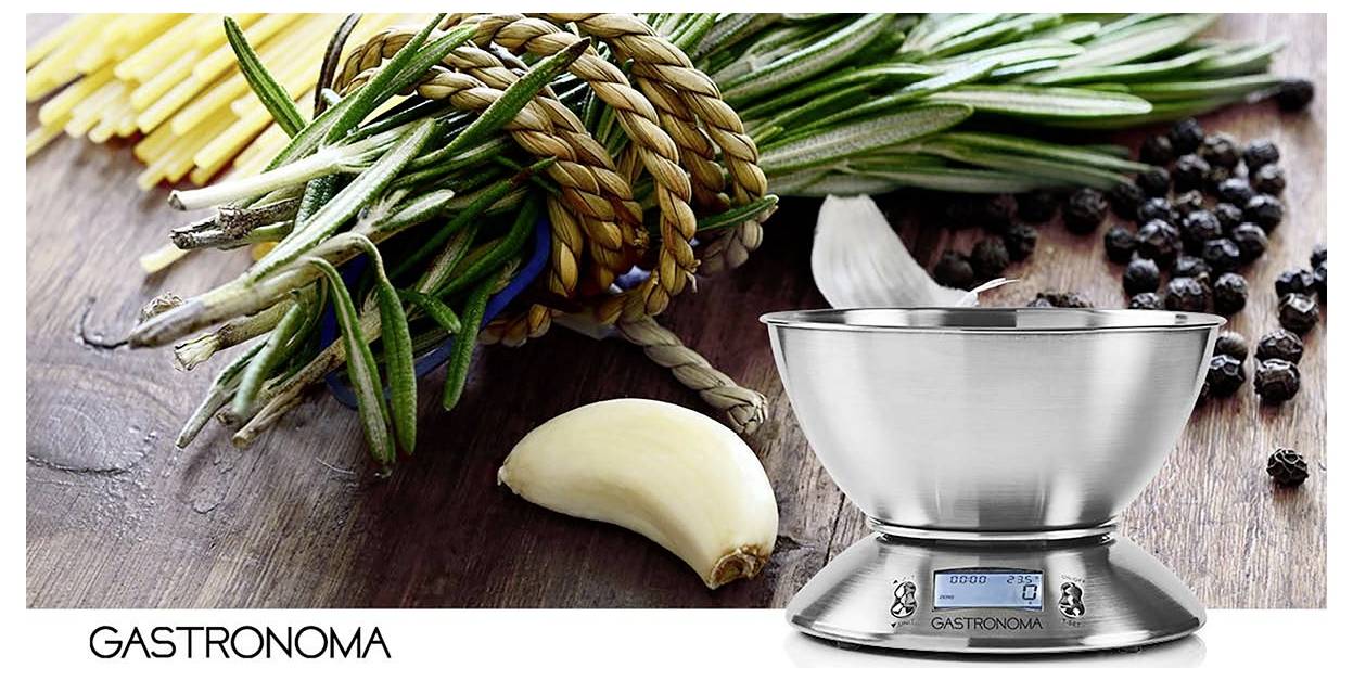 Eine Küchenwaage aus Metall auf einer Holzoberfläche mit Kräutern, Knoblauch und Pfefferkörnern. Markenname 'Gastronoma' ist sichtbar.