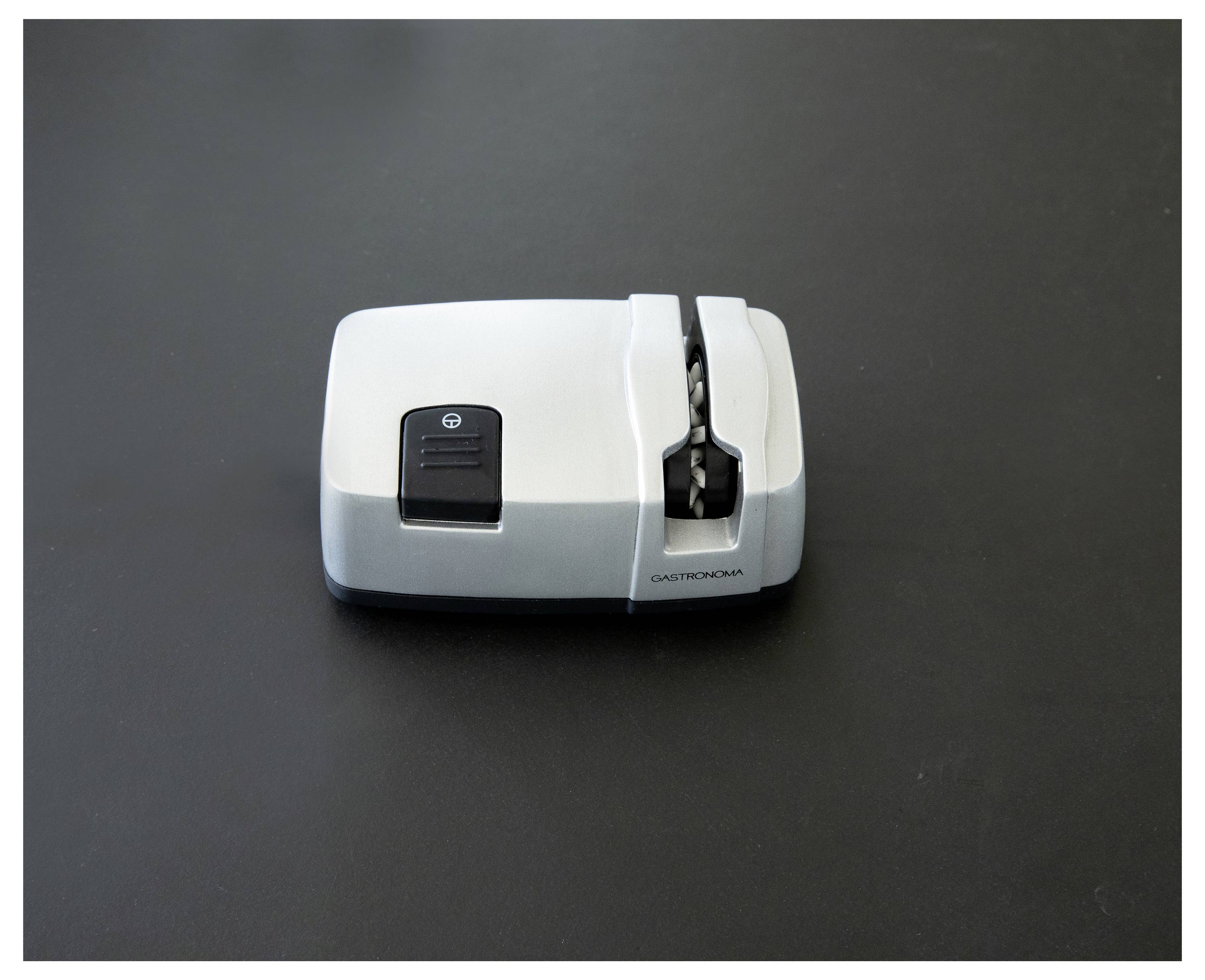 Ein weiß-grauer elektrischer Anspitzer auf einer dunklen Oberfläche, der sein schlankes Design und seine Funktionalität mit einem sichtbaren Einschaltknopf präsentiert.